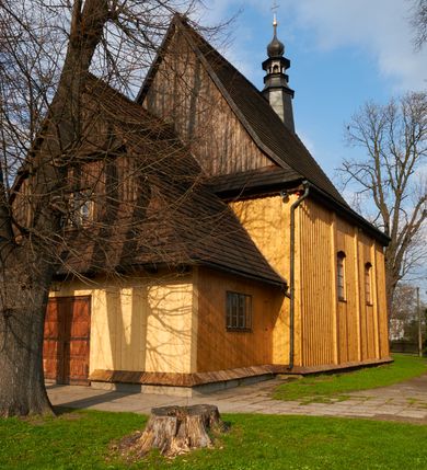 Zdjęcie nr 44: Kościół drewniany o konstrukcji zrębowej, na betonowym podmurowaniu przesłoniętym daszkiem gontowym, kruchta zachodnia o konstrukcji słupowo-ramowej. Elewacje jednolite, szalowane z listwowaniem, wzmocnione lisicami. Więźba dachowa drewniana, krokwiowa. Kościół orientowany, jednonawowy, nawa na rzucie prostokąta zbliżonego do kwadratu, prezbiterium nieco węższe, zakończone trójbocznie. Do wschodniej ściany prezbiterium przylega Ogrójec na rzucie prostokąta, od północy zakrystia na planie zbliżonym do trapezu. Do północnej ściany nawy przylega niewielka kruchta na rzucie prostokąta, od zachodu duża kruchta na planie prostokąta z pomieszczeniem nad nią, ze schodami drabiniastymi na chór, otwarta do nawy trzema dużymi otworami o wykroju prostokątnym. Wnętrze podzielone pilastrami podtrzymującymi architraw i fryz, wyłamane na ich osi. Pomiędzy nawą a prezbiterium prostokątny otwór tęczowy z prostą belką. Parapet chóru muzycznego w zachodniej części nawy, o wklęsło-wypukłym zarysie, podparty przez dwie kolumny i dwie półkolumny o wielobocznych trzonach. Otwory drzwiowe o prostokątnym wykroju zamknięte drzwiami spągowymi w północnej ścianie nawy oraz prezbiterium. Wnętrze nakryte pułapami deskowymi. Posadzka z płyt ceramicznych. 
Elewacja frontowa jednoosiowa, na osi wejście do kruchty z dwuskrzydłowymi drzwiami, w partii szczytu podwójne okno. W elewacji południowej cztery otwory okienne w formie stojącego prostokąta zamkniętego łukiem odcinkowym, dwa w nawie i dwa w prezbiterium oraz prostokątne, podwójne okno w kruchcie zachodniej, z krosnowymi oknami o drobnych podziałach kwaterowych. Elewacja północna z prostokątnym, podwójnym oknem w części kruchty zachodniej oraz z wejściami do kruchty północnej i do zakrystii o dwuskrzydłowych drzwiach. Na ścianie wschodniej prezbiterium Ogrójec w formie głębokiej szalowanej wnęki przesłoniętej daszkiem pulpitowym. Kościół nakryty dachami gontowymi dwuspadowymi, wyższym nad nawą, niższym nad prezbiterium, z kalenicą dekorowaną gontowym grzebieniem, nad zakrystią i kruchtą północną miękko modelowane dachy trójspadowe, kruchta zachodnia nakryta dachem dwuspadowym, półszczytowym. W połowie długości dachu nad nawą od strony prezbiterium wznosi się ponad kalenicą wieżyczka na sygnaturkę, na ośmiobocznym obitym blachą trzonie, z latarnią zwieńczoną niewielkim cebulastym hełmem.

 

