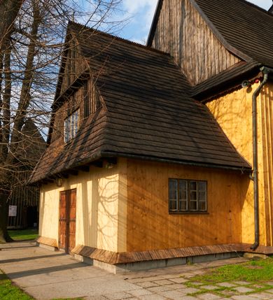 Zdjęcie nr 46: Kościół drewniany o konstrukcji zrębowej, na betonowym podmurowaniu przesłoniętym daszkiem gontowym, kruchta zachodnia o konstrukcji słupowo-ramowej. Elewacje jednolite, szalowane z listwowaniem, wzmocnione lisicami. Więźba dachowa drewniana, krokwiowa. Kościół orientowany, jednonawowy, nawa na rzucie prostokąta zbliżonego do kwadratu, prezbiterium nieco węższe, zakończone trójbocznie. Do wschodniej ściany prezbiterium przylega Ogrójec na rzucie prostokąta, od północy zakrystia na planie zbliżonym do trapezu. Do północnej ściany nawy przylega niewielka kruchta na rzucie prostokąta, od zachodu duża kruchta na planie prostokąta z pomieszczeniem nad nią, ze schodami drabiniastymi na chór, otwarta do nawy trzema dużymi otworami o wykroju prostokątnym. Wnętrze podzielone pilastrami podtrzymującymi architraw i fryz, wyłamane na ich osi. Pomiędzy nawą a prezbiterium prostokątny otwór tęczowy z prostą belką. Parapet chóru muzycznego w zachodniej części nawy, o wklęsło-wypukłym zarysie, podparty przez dwie kolumny i dwie półkolumny o wielobocznych trzonach. Otwory drzwiowe o prostokątnym wykroju zamknięte drzwiami spągowymi w północnej ścianie nawy oraz prezbiterium. Wnętrze nakryte pułapami deskowymi. Posadzka z płyt ceramicznych. 
Elewacja frontowa jednoosiowa, na osi wejście do kruchty z dwuskrzydłowymi drzwiami, w partii szczytu podwójne okno. W elewacji południowej cztery otwory okienne w formie stojącego prostokąta zamkniętego łukiem odcinkowym, dwa w nawie i dwa w prezbiterium oraz prostokątne, podwójne okno w kruchcie zachodniej, z krosnowymi oknami o drobnych podziałach kwaterowych. Elewacja północna z prostokątnym, podwójnym oknem w części kruchty zachodniej oraz z wejściami do kruchty północnej i do zakrystii o dwuskrzydłowych drzwiach. Na ścianie wschodniej prezbiterium Ogrójec w formie głębokiej szalowanej wnęki przesłoniętej daszkiem pulpitowym. Kościół nakryty dachami gontowymi dwuspadowymi, wyższym nad nawą, niższym nad prezbiterium, z kalenicą dekorowaną gontowym grzebieniem, nad zakrystią i kruchtą północną miękko modelowane dachy trójspadowe, kruchta zachodnia nakryta dachem dwuspadowym, półszczytowym. W połowie długości dachu nad nawą od strony prezbiterium wznosi się ponad kalenicą wieżyczka na sygnaturkę, na ośmiobocznym obitym blachą trzonie, z latarnią zwieńczoną niewielkim cebulastym hełmem.

 

