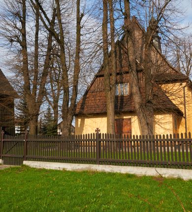 Zdjęcie nr 56: Kościół drewniany o konstrukcji zrębowej, na betonowym podmurowaniu przesłoniętym daszkiem gontowym, kruchta zachodnia o konstrukcji słupowo-ramowej. Elewacje jednolite, szalowane z listwowaniem, wzmocnione lisicami. Więźba dachowa drewniana, krokwiowa. Kościół orientowany, jednonawowy, nawa na rzucie prostokąta zbliżonego do kwadratu, prezbiterium nieco węższe, zakończone trójbocznie. Do wschodniej ściany prezbiterium przylega Ogrójec na rzucie prostokąta, od północy zakrystia na planie zbliżonym do trapezu. Do północnej ściany nawy przylega niewielka kruchta na rzucie prostokąta, od zachodu duża kruchta na planie prostokąta z pomieszczeniem nad nią, ze schodami drabiniastymi na chór, otwarta do nawy trzema dużymi otworami o wykroju prostokątnym. Wnętrze podzielone pilastrami podtrzymującymi architraw i fryz, wyłamane na ich osi. Pomiędzy nawą a prezbiterium prostokątny otwór tęczowy z prostą belką. Parapet chóru muzycznego w zachodniej części nawy, o wklęsło-wypukłym zarysie, podparty przez dwie kolumny i dwie półkolumny o wielobocznych trzonach. Otwory drzwiowe o prostokątnym wykroju zamknięte drzwiami spągowymi w północnej ścianie nawy oraz prezbiterium. Wnętrze nakryte pułapami deskowymi. Posadzka z płyt ceramicznych. 
Elewacja frontowa jednoosiowa, na osi wejście do kruchty z dwuskrzydłowymi drzwiami, w partii szczytu podwójne okno. W elewacji południowej cztery otwory okienne w formie stojącego prostokąta zamkniętego łukiem odcinkowym, dwa w nawie i dwa w prezbiterium oraz prostokątne, podwójne okno w kruchcie zachodniej, z krosnowymi oknami o drobnych podziałach kwaterowych. Elewacja północna z prostokątnym, podwójnym oknem w części kruchty zachodniej oraz z wejściami do kruchty północnej i do zakrystii o dwuskrzydłowych drzwiach. Na ścianie wschodniej prezbiterium Ogrójec w formie głębokiej szalowanej wnęki przesłoniętej daszkiem pulpitowym. Kościół nakryty dachami gontowymi dwuspadowymi, wyższym nad nawą, niższym nad prezbiterium, z kalenicą dekorowaną gontowym grzebieniem, nad zakrystią i kruchtą północną miękko modelowane dachy trójspadowe, kruchta zachodnia nakryta dachem dwuspadowym, półszczytowym. W połowie długości dachu nad nawą od strony prezbiterium wznosi się ponad kalenicą wieżyczka na sygnaturkę, na ośmiobocznym obitym blachą trzonie, z latarnią zwieńczoną niewielkim cebulastym hełmem.

 

