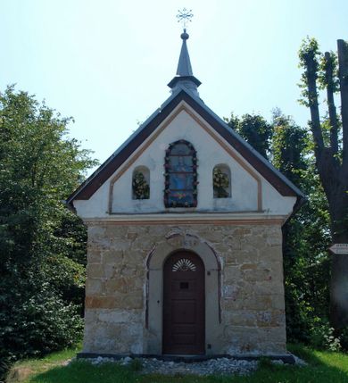 Zdjęcie nr 1: Kapliczkaa przydrożna, usytuowana przy szosie z Koźmic do Dobczyc, frontem zwrócona na północ, na planie prostokąta zbliżonego do kwadratu, zakończonego półkolista absydą. Przykryta dachem dwuspadowym, krytym blachą; z sygnaturką iglicową i z kulą zwieńczoną metalowym krzyżem. Fasada z prostym, trójkątnym szczytem i z prostokątnymi niszami zamkniętymi półkoliście. W środkowej, przeszklonej niszy umieszczona jest figura Matki Boskiej. Portal kamienny, zamknięty łukiem półkolistym z wyrytą na osi datą „1868 R.”. Drzwi jednoskrzydłowe, dubeltowe o zewnętrznej warstwie płycinowej z polichromowanym reliefem, przedstawiającym Oko Opatrzności. Pośrodku antaba żelazna; zawiasy kowalskie. Okna przeszklone, wielokwaterowe. Wnętrze jednoprzestrzenne z cementową posadzką (obecnie puste, kaplica jest w trakcie remontu). Na wyposażaniu ołtarz Matki Boskiej Różańcowej, figura św. Jana Nepomucena i drewniane, ludowe lichtarze.