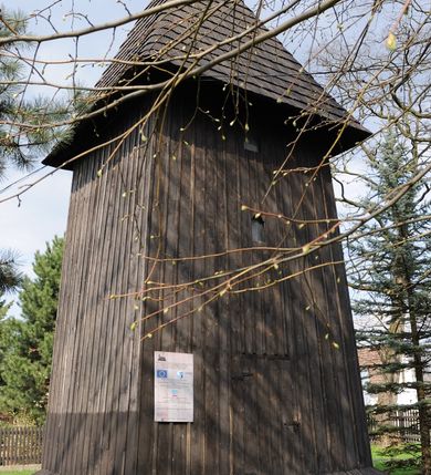 Zdjęcie nr 3: Dzwonnica drewniana, konstrukcji słupowej, ściany szalowane z listowaniem, więźba dachowa drewniana. Założona na planie prostokąta zbliżonego do kwadratu, na betonowym podmurowaniu, przesłoniętym okapowym daszkiem gontowym. Dach gontowy, czterospadowy, zakończony metalowym szpikulcem. Otwór drzwiowy w ścianie południowej o wykroju stojącego prostokąta zamknięty drzwiami spągowymi. Niewielkie otwory głosowe w formie stojącego prostokąta zamkniętego łukiem półkolistym nadwieszonym po dwa na południowej, wschodniej i północnej ścianie. Wnętrze wypełnione elementami konstrukcji.
