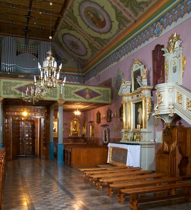 Zdjęcie nr 17: Kościół położony pośrodku wsi, na wysokiej skarpie, wzmocnionej murem. Otoczenie ogrodzone współcześnie. Od wschodu dzwonnica w formie bramy, ze schodami.  Kościół murowany, tynkowany, orientowany, zbudowany na planie wydłużonego prostokąta, jednonawowy, z węższym prezbiterium zamkniętym wielobocznie, opiętym szkarpami. Od północy przylega parterowa zakrystia z przedsionkiem, od południa dwie kruchty. Nawa od prezbiterium oddzielone ostrołukową arkadą. Wnętrze oświetlone oknami prostokątnymi zamkniętymi odcinkowo, wszystkie z witrażami. Nawa nakryta trójspadowym stropem, prezbiterium sklepieniem krzyżowo-żebrowym. Odrzwia z prezbiterium do zakrystii ostrołukowe. Okno w prezbiterium od wschodu ostrołukowe (zamurowane), okno w przedsionku zamknięte tzw. oślim grzbietem. Elewacje na kamiennym, obecnie tynkowanym cokole, oszkarpowane. Szkarpy uskokowe o zmiennym przekroju. Fasada jednoosiowa, zwieńczona trójkątnym szczytem. W osi elewacji ostrołukowy profilowany uskokowo portal, w szczycie okrągły otwór okienny, w płaskiej, tynkowanej opasce. Szczyt dodatkowo podzielony lizenami, u góry zdobiony fryzem arkadkowym, zamknięty wydatnym, profilowanym gzymsem. Oś elewacji zaakcentowana pośrodku wykonanym w tynku i zróżnicowanym kolorystycznie krzyżem, umieszczonym nad wejściem. Po lewej stronie portalu marmurowa tablica epitafijna. Po prawej stronie portalu marmurowa prostokątna tablica z donatorami. Elewacja zachodnia zamknięta wielobocznie, oszkarpowana. W górnej części ostrołukowa blenda, poniżej umieszczony krucyfiks, osłonięty dwuspadowym daszkiem, wspartym na konsolkach. Elewacje boczne pięcioosiowe z prostokątnymi otworami drzwiowymi w drugich osiach od zachodu. Poszczególne osie oddzielone prostokątnymi oknami. Zakrystia i kruchty nakryte dachem jednospadowym. Konstrukcja dachu korpusu głównego drewniana, krokwiowo-płatwiowa. Dach dwuspadowy, nad prezbiterium trójspadowy, kryty blachą ocynkowaną. Sygnaturka w całości obita blachą. Dzwonnica posiada dwie kondygnacje: dolną przeprutą dwiema arkadami, tworzącymi wejście w obręb cmentarza kościelnego i górną, przedzieloną czterema arkadami, przeznaczonymi na pomieszczenie dzwonów. Dach siodłowy.
