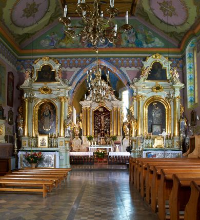 Zdjęcie nr 12: Kościół położony pośrodku wsi, na wysokiej skarpie, wzmocnionej murem. Otoczenie ogrodzone współcześnie. Od wschodu dzwonnica w formie bramy, ze schodami.  Kościół murowany, tynkowany, orientowany, zbudowany na planie wydłużonego prostokąta, jednonawowy, z węższym prezbiterium zamkniętym wielobocznie, opiętym szkarpami. Od północy przylega parterowa zakrystia z przedsionkiem, od południa dwie kruchty. Nawa od prezbiterium oddzielone ostrołukową arkadą. Wnętrze oświetlone oknami prostokątnymi zamkniętymi odcinkowo, wszystkie z witrażami. Nawa nakryta trójspadowym stropem, prezbiterium sklepieniem krzyżowo-żebrowym. Odrzwia z prezbiterium do zakrystii ostrołukowe. Okno w prezbiterium od wschodu ostrołukowe (zamurowane), okno w przedsionku zamknięte tzw. oślim grzbietem. Elewacje na kamiennym, obecnie tynkowanym cokole, oszkarpowane. Szkarpy uskokowe o zmiennym przekroju. Fasada jednoosiowa, zwieńczona trójkątnym szczytem. W osi elewacji ostrołukowy profilowany uskokowo portal, w szczycie okrągły otwór okienny, w płaskiej, tynkowanej opasce. Szczyt dodatkowo podzielony lizenami, u góry zdobiony fryzem arkadkowym, zamknięty wydatnym, profilowanym gzymsem. Oś elewacji zaakcentowana pośrodku wykonanym w tynku i zróżnicowanym kolorystycznie krzyżem, umieszczonym nad wejściem. Po lewej stronie portalu marmurowa tablica epitafijna. Po prawej stronie portalu marmurowa prostokątna tablica z donatorami. Elewacja zachodnia zamknięta wielobocznie, oszkarpowana. W górnej części ostrołukowa blenda, poniżej umieszczony krucyfiks, osłonięty dwuspadowym daszkiem, wspartym na konsolkach. Elewacje boczne pięcioosiowe z prostokątnymi otworami drzwiowymi w drugich osiach od zachodu. Poszczególne osie oddzielone prostokątnymi oknami. Zakrystia i kruchty nakryte dachem jednospadowym. Konstrukcja dachu korpusu głównego drewniana, krokwiowo-płatwiowa. Dach dwuspadowy, nad prezbiterium trójspadowy, kryty blachą ocynkowaną. Sygnaturka w całości obita blachą. Dzwonnica posiada dwie kondygnacje: dolną przeprutą dwiema arkadami, tworzącymi wejście w obręb cmentarza kościelnego i górną, przedzieloną czterema arkadami, przeznaczonymi na pomieszczenie dzwonów. Dach siodłowy.
