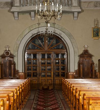 Zdjęcie nr 26: Kościół pw. Opieki Matki Boskiej w Kamieniu usytuowany jest na niewielkiej, wydzielonej ogrodzeniem działce usytuowanej na południe od głównej drogi wiodącej przez miejscowość. Kamieński kościół to budowla murowana z kamienia i cegły, orientowana, jednonawowa z nawą na rzucie prostokąta opiętą dziesięcioma trójuskokowymi przyporami oraz nieco węższym i półokrągło zamkniętym prezbiterium. Od strony północnej do prezbiterium przylega zakrystia na planie prostokąta. Do północno-zachodniej części nawy dostawiona jest niewielka, prostokątna kruchta. Wnętrze świątyni sklepiono sklepieniem kolebkowym z lunetami. Nawę i prezbiterium nakrywają dachy dwuspadowe, natomiast wieżę dach ostrosłupowy o czterech połaciach zwieńczony niewielkim krzyżem. Pierwotnie świątynia przekryta była dachem z czerwonej dachówki, którą w 1985 roku wymieniono na obecne pokrycie z ocynkowanej blachy. Więźbę dachową o konstrukcji płatwiowo-kleszczowej z krzyżującymi się stolcami wykonano z drewna sosnowego. Do wnętrza świątyni prowadzą trzy wejścia – główne z kruchtą od strony zachodniej, boczne również z kruchtą, z której wychodzi się na chór muzyczny i wieżę od strony północnej oraz wejście przez zakrystię. Do wejścia głównego prowadziły masywne, betonowe schody na rzucie półokręgu wylane w 1928 roku, które w 1981 roku zostały zastąpione obecnymi schodami na rzucie prostokąta. W trójosiowej i trójkondygnacyjnej fasadzie świątyni zaakcentowana wysunięciem do przodu jest oś środkowa przechodząca w górnej części w czworoboczną wieżę. W jej pierwszej kondygnacji mieści się zadaszony, opracowany w cegle, neobarokowy portal główny. Wieńczy go gzyms o kształcie łuku kotarowego, na szczycie którego znajduje się krzyż. W portalu umieszczone są dwuskrzydłowe, drewniane drzwi zamknięte łukiem półokrągłym. Ponad otworem wejściowym, w osi portalu znajduje się przeszklona rozeta. W kondygnacjach drugiej i trzeciej omawianej osi środkowej fasady mieszczą się półkoliście zamknięte okna. W osiach skrajnych nieregularnie rozmieszczono niewielkie, prostokątne okna, w kondygnacji pierwszej zamknięte półkoliście. Elewacje boczne świątyni są czteroosiowe i jednokondygnacyjne, z wyjątkiem trzykondygnacyjnej osi pierwszej, w której od strony północnej mieści się prostokątna kruchta, ponad którą rozmieszczono dwa półokrągło zamknięte okna, po jednym w kondygnacji drugiej i trzeciej. Od strony południowej we wszystkich kondygnacjach mieszczą się półokrągłe okna. Elewacje boczne nawy artykułowane są przyporami, pomiędzy którymi znajdują się okna zamknięte łukiem półokrągłym. W prezbiterium od strony wschodniej mieszczą się dwa półokrągłe okna.