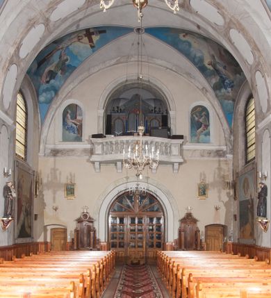 Zdjęcie nr 19: Kościół pw. Opieki Matki Boskiej w Kamieniu usytuowany jest na niewielkiej, wydzielonej ogrodzeniem działce usytuowanej na południe od głównej drogi wiodącej przez miejscowość. Kamieński kościół to budowla murowana z kamienia i cegły, orientowana, jednonawowa z nawą na rzucie prostokąta opiętą dziesięcioma trójuskokowymi przyporami oraz nieco węższym i półokrągło zamkniętym prezbiterium. Od strony północnej do prezbiterium przylega zakrystia na planie prostokąta. Do północno-zachodniej części nawy dostawiona jest niewielka, prostokątna kruchta. Wnętrze świątyni sklepiono sklepieniem kolebkowym z lunetami. Nawę i prezbiterium nakrywają dachy dwuspadowe, natomiast wieżę dach ostrosłupowy o czterech połaciach zwieńczony niewielkim krzyżem. Pierwotnie świątynia przekryta była dachem z czerwonej dachówki, którą w 1985 roku wymieniono na obecne pokrycie z ocynkowanej blachy. Więźbę dachową o konstrukcji płatwiowo-kleszczowej z krzyżującymi się stolcami wykonano z drewna sosnowego. Do wnętrza świątyni prowadzą trzy wejścia – główne z kruchtą od strony zachodniej, boczne również z kruchtą, z której wychodzi się na chór muzyczny i wieżę od strony północnej oraz wejście przez zakrystię. Do wejścia głównego prowadziły masywne, betonowe schody na rzucie półokręgu wylane w 1928 roku, które w 1981 roku zostały zastąpione obecnymi schodami na rzucie prostokąta. W trójosiowej i trójkondygnacyjnej fasadzie świątyni zaakcentowana wysunięciem do przodu jest oś środkowa przechodząca w górnej części w czworoboczną wieżę. W jej pierwszej kondygnacji mieści się zadaszony, opracowany w cegle, neobarokowy portal główny. Wieńczy go gzyms o kształcie łuku kotarowego, na szczycie którego znajduje się krzyż. W portalu umieszczone są dwuskrzydłowe, drewniane drzwi zamknięte łukiem półokrągłym. Ponad otworem wejściowym, w osi portalu znajduje się przeszklona rozeta. W kondygnacjach drugiej i trzeciej omawianej osi środkowej fasady mieszczą się półkoliście zamknięte okna. W osiach skrajnych nieregularnie rozmieszczono niewielkie, prostokątne okna, w kondygnacji pierwszej zamknięte półkoliście. Elewacje boczne świątyni są czteroosiowe i jednokondygnacyjne, z wyjątkiem trzykondygnacyjnej osi pierwszej, w której od strony północnej mieści się prostokątna kruchta, ponad którą rozmieszczono dwa półokrągło zamknięte okna, po jednym w kondygnacji drugiej i trzeciej. Od strony południowej we wszystkich kondygnacjach mieszczą się półokrągłe okna. Elewacje boczne nawy artykułowane są przyporami, pomiędzy którymi znajdują się okna zamknięte łukiem półokrągłym. W prezbiterium od strony wschodniej mieszczą się dwa półokrągłe okna.