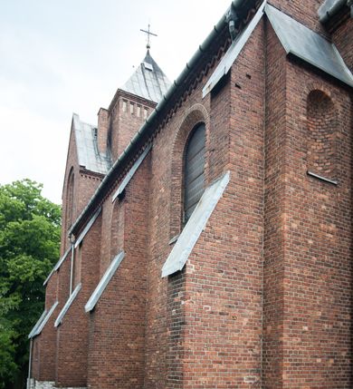 Zdjęcie nr 33: Kościół pw. Opieki Matki Boskiej w Kamieniu usytuowany jest na niewielkiej, wydzielonej ogrodzeniem działce usytuowanej na południe od głównej drogi wiodącej przez miejscowość. Kamieński kościół to budowla murowana z kamienia i cegły, orientowana, jednonawowa z nawą na rzucie prostokąta opiętą dziesięcioma trójuskokowymi przyporami oraz nieco węższym i półokrągło zamkniętym prezbiterium. Od strony północnej do prezbiterium przylega zakrystia na planie prostokąta. Do północno-zachodniej części nawy dostawiona jest niewielka, prostokątna kruchta. Wnętrze świątyni sklepiono sklepieniem kolebkowym z lunetami. Nawę i prezbiterium nakrywają dachy dwuspadowe, natomiast wieżę dach ostrosłupowy o czterech połaciach zwieńczony niewielkim krzyżem. Pierwotnie świątynia przekryta była dachem z czerwonej dachówki, którą w 1985 roku wymieniono na obecne pokrycie z ocynkowanej blachy. Więźbę dachową o konstrukcji płatwiowo-kleszczowej z krzyżującymi się stolcami wykonano z drewna sosnowego. Do wnętrza świątyni prowadzą trzy wejścia – główne z kruchtą od strony zachodniej, boczne również z kruchtą, z której wychodzi się na chór muzyczny i wieżę od strony północnej oraz wejście przez zakrystię. Do wejścia głównego prowadziły masywne, betonowe schody na rzucie półokręgu wylane w 1928 roku, które w 1981 roku zostały zastąpione obecnymi schodami na rzucie prostokąta. W trójosiowej i trójkondygnacyjnej fasadzie świątyni zaakcentowana wysunięciem do przodu jest oś środkowa przechodząca w górnej części w czworoboczną wieżę. W jej pierwszej kondygnacji mieści się zadaszony, opracowany w cegle, neobarokowy portal główny. Wieńczy go gzyms o kształcie łuku kotarowego, na szczycie którego znajduje się krzyż. W portalu umieszczone są dwuskrzydłowe, drewniane drzwi zamknięte łukiem półokrągłym. Ponad otworem wejściowym, w osi portalu znajduje się przeszklona rozeta. W kondygnacjach drugiej i trzeciej omawianej osi środkowej fasady mieszczą się półkoliście zamknięte okna. W osiach skrajnych nieregularnie rozmieszczono niewielkie, prostokątne okna, w kondygnacji pierwszej zamknięte półkoliście. Elewacje boczne świątyni są czteroosiowe i jednokondygnacyjne, z wyjątkiem trzykondygnacyjnej osi pierwszej, w której od strony północnej mieści się prostokątna kruchta, ponad którą rozmieszczono dwa półokrągło zamknięte okna, po jednym w kondygnacji drugiej i trzeciej. Od strony południowej we wszystkich kondygnacjach mieszczą się półokrągłe okna. Elewacje boczne nawy artykułowane są przyporami, pomiędzy którymi znajdują się okna zamknięte łukiem półokrągłym. W prezbiterium od strony wschodniej mieszczą się dwa półokrągłe okna.