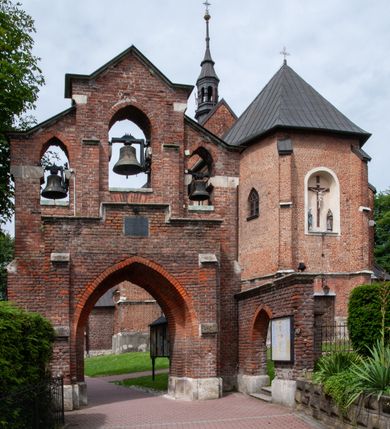 Zdjęcie nr 7: Kościół jest zlokalizowany na wzgórzu, w centrum wsi. Murowany z cegły, w wątku polskim, z zendrówką. Kościół jest orientowany, założony na planie prostokąta, jednonawowy, trójprzęsłowy, z dobudowanymi kruchtami od zachodu i południa. Prezbiterium oddzielone od nawy łukiem tęczowym, dwuprzęsłowe na planie prostokąta, zamknięte prostą ścianą, z dwukondygnacyjną przybudówką zakończoną trójbocznie. Nawa została przykryta sklepieniem sieciowym. Ściana południowa nawy przepruta trzema prostokątnymi oknami, zamkniętymi łukiem ostrym. Okna w nawie i prezbiterium dwudzielne, z sześcioma mniejszymi kwaterami. Przybudówka przy prezbiterium na parterze mieści zakrystię, a na piętrze składzik. Kruchta południowa sklepiona kolebką. Z kruchty do nawy prowadzi ostrołukowy, kamienny portal o dwóch archiwoltach. Kruchta zachodnia, obecnie kaplica św. Franciszka, sklepiona spłaszczoną, ukrytą kopułą na pendentywach. Ściana zachodnia kruchty przepruta dwoma ostrołukowymi oknami i ponad nimi okrągłym oknem. Od południa ostrołukowe wejście. Kościół o zróżnicowanej wysokości nawy i prezbiterium. Ściany opięte szkarpami. Na jednej trzeciej wysokości ścian oraz w zwieńczeniu nawy i prezbiterium profilowany gzyms. Od zachodu wklęsło-wypukły szczyt. Nawa, prezbiterium i dwie kruchty przykryte dachem dwuspadowym. Nad drugim przęsłem prezbiterium wieżyczka na sygnaturkę na planie ośmioboku, z profilowanym gzymsem i latarnią, zwieńczoną hełmem z kulą i krzyżem. Wejście do kościoła od południa i zachodu. Okna nawy i prezbiterium z kamiennym obramieniem. Nad wejściem do kruchty południowej formowany w cegle ostry łuk. Analogiczny łuk nad oknami w ścianie zachodniej i nad blendą w ścianie północnej. W przybudówce do prezbiterium dwie kondygnacje okien zamkniętych łukiem ostrym. W ścianie frontowej prostokątne wejście, a nad nim półkoliście zamknięta wnęka z grupą Ukrzyżowania. 


