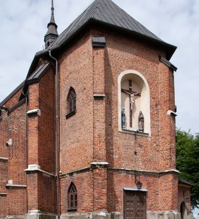 Zdjęcie nr 20: Kościół jest zlokalizowany na wzgórzu, w centrum wsi. Murowany z cegły, w wątku polskim, z zendrówką. Kościół jest orientowany, założony na planie prostokąta, jednonawowy, trójprzęsłowy, z dobudowanymi kruchtami od zachodu i południa. Prezbiterium oddzielone od nawy łukiem tęczowym, dwuprzęsłowe na planie prostokąta, zamknięte prostą ścianą, z dwukondygnacyjną przybudówką zakończoną trójbocznie. Nawa została przykryta sklepieniem sieciowym. Ściana południowa nawy przepruta trzema prostokątnymi oknami, zamkniętymi łukiem ostrym. Okna w nawie i prezbiterium dwudzielne, z sześcioma mniejszymi kwaterami. Przybudówka przy prezbiterium na parterze mieści zakrystię, a na piętrze składzik. Kruchta południowa sklepiona kolebką. Z kruchty do nawy prowadzi ostrołukowy, kamienny portal o dwóch archiwoltach. Kruchta zachodnia, obecnie kaplica św. Franciszka, sklepiona spłaszczoną, ukrytą kopułą na pendentywach. Ściana zachodnia kruchty przepruta dwoma ostrołukowymi oknami i ponad nimi okrągłym oknem. Od południa ostrołukowe wejście. Kościół o zróżnicowanej wysokości nawy i prezbiterium. Ściany opięte szkarpami. Na jednej trzeciej wysokości ścian oraz w zwieńczeniu nawy i prezbiterium profilowany gzyms. Od zachodu wklęsło-wypukły szczyt. Nawa, prezbiterium i dwie kruchty przykryte dachem dwuspadowym. Nad drugim przęsłem prezbiterium wieżyczka na sygnaturkę na planie ośmioboku, z profilowanym gzymsem i latarnią, zwieńczoną hełmem z kulą i krzyżem. Wejście do kościoła od południa i zachodu. Okna nawy i prezbiterium z kamiennym obramieniem. Nad wejściem do kruchty południowej formowany w cegle ostry łuk. Analogiczny łuk nad oknami w ścianie zachodniej i nad blendą w ścianie północnej. W przybudówce do prezbiterium dwie kondygnacje okien zamkniętych łukiem ostrym. W ścianie frontowej prostokątne wejście, a nad nim półkoliście zamknięta wnęka z grupą Ukrzyżowania. 


