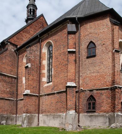 Zdjęcie nr 23: Kościół jest zlokalizowany na wzgórzu, w centrum wsi. Murowany z cegły, w wątku polskim, z zendrówką. Kościół jest orientowany, założony na planie prostokąta, jednonawowy, trójprzęsłowy, z dobudowanymi kruchtami od zachodu i południa. Prezbiterium oddzielone od nawy łukiem tęczowym, dwuprzęsłowe na planie prostokąta, zamknięte prostą ścianą, z dwukondygnacyjną przybudówką zakończoną trójbocznie. Nawa została przykryta sklepieniem sieciowym. Ściana południowa nawy przepruta trzema prostokątnymi oknami, zamkniętymi łukiem ostrym. Okna w nawie i prezbiterium dwudzielne, z sześcioma mniejszymi kwaterami. Przybudówka przy prezbiterium na parterze mieści zakrystię, a na piętrze składzik. Kruchta południowa sklepiona kolebką. Z kruchty do nawy prowadzi ostrołukowy, kamienny portal o dwóch archiwoltach. Kruchta zachodnia, obecnie kaplica św. Franciszka, sklepiona spłaszczoną, ukrytą kopułą na pendentywach. Ściana zachodnia kruchty przepruta dwoma ostrołukowymi oknami i ponad nimi okrągłym oknem. Od południa ostrołukowe wejście. Kościół o zróżnicowanej wysokości nawy i prezbiterium. Ściany opięte szkarpami. Na jednej trzeciej wysokości ścian oraz w zwieńczeniu nawy i prezbiterium profilowany gzyms. Od zachodu wklęsło-wypukły szczyt. Nawa, prezbiterium i dwie kruchty przykryte dachem dwuspadowym. Nad drugim przęsłem prezbiterium wieżyczka na sygnaturkę na planie ośmioboku, z profilowanym gzymsem i latarnią, zwieńczoną hełmem z kulą i krzyżem. Wejście do kościoła od południa i zachodu. Okna nawy i prezbiterium z kamiennym obramieniem. Nad wejściem do kruchty południowej formowany w cegle ostry łuk. Analogiczny łuk nad oknami w ścianie zachodniej i nad blendą w ścianie północnej. W przybudówce do prezbiterium dwie kondygnacje okien zamkniętych łukiem ostrym. W ścianie frontowej prostokątne wejście, a nad nim półkoliście zamknięta wnęka z grupą Ukrzyżowania. 


