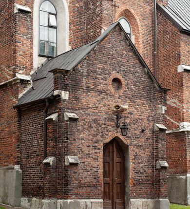 Zdjęcie nr 43: Kościół jest zlokalizowany na wzgórzu, w centrum wsi. Murowany z cegły, w wątku polskim, z zendrówką. Kościół jest orientowany, założony na planie prostokąta, jednonawowy, trójprzęsłowy, z dobudowanymi kruchtami od zachodu i południa. Prezbiterium oddzielone od nawy łukiem tęczowym, dwuprzęsłowe na planie prostokąta, zamknięte prostą ścianą, z dwukondygnacyjną przybudówką zakończoną trójbocznie. Nawa została przykryta sklepieniem sieciowym. Ściana południowa nawy przepruta trzema prostokątnymi oknami, zamkniętymi łukiem ostrym. Okna w nawie i prezbiterium dwudzielne, z sześcioma mniejszymi kwaterami. Przybudówka przy prezbiterium na parterze mieści zakrystię, a na piętrze składzik. Kruchta południowa sklepiona kolebką. Z kruchty do nawy prowadzi ostrołukowy, kamienny portal o dwóch archiwoltach. Kruchta zachodnia, obecnie kaplica św. Franciszka, sklepiona spłaszczoną, ukrytą kopułą na pendentywach. Ściana zachodnia kruchty przepruta dwoma ostrołukowymi oknami i ponad nimi okrągłym oknem. Od południa ostrołukowe wejście. Kościół o zróżnicowanej wysokości nawy i prezbiterium. Ściany opięte szkarpami. Na jednej trzeciej wysokości ścian oraz w zwieńczeniu nawy i prezbiterium profilowany gzyms. Od zachodu wklęsło-wypukły szczyt. Nawa, prezbiterium i dwie kruchty przykryte dachem dwuspadowym. Nad drugim przęsłem prezbiterium wieżyczka na sygnaturkę na planie ośmioboku, z profilowanym gzymsem i latarnią, zwieńczoną hełmem z kulą i krzyżem. Wejście do kościoła od południa i zachodu. Okna nawy i prezbiterium z kamiennym obramieniem. Nad wejściem do kruchty południowej formowany w cegle ostry łuk. Analogiczny łuk nad oknami w ścianie zachodniej i nad blendą w ścianie północnej. W przybudówce do prezbiterium dwie kondygnacje okien zamkniętych łukiem ostrym. W ścianie frontowej prostokątne wejście, a nad nim półkoliście zamknięta wnęka z grupą Ukrzyżowania. 


