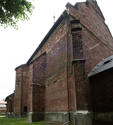 Zdjęcie nr 56: Kościół jest zlokalizowany na wzgórzu, w centrum wsi. Murowany z cegły, w wątku polskim, z zendrówką. Kościół jest orientowany, założony na planie prostokąta, jednonawowy, trójprzęsłowy, z dobudowanymi kruchtami od zachodu i południa. Prezbiterium oddzielone od nawy łukiem tęczowym, dwuprzęsłowe na planie prostokąta, zamknięte prostą ścianą, z dwukondygnacyjną przybudówką zakończoną trójbocznie. Nawa została przykryta sklepieniem sieciowym. Ściana południowa nawy przepruta trzema prostokątnymi oknami, zamkniętymi łukiem ostrym. Okna w nawie i prezbiterium dwudzielne, z sześcioma mniejszymi kwaterami. Przybudówka przy prezbiterium na parterze mieści zakrystię, a na piętrze składzik. Kruchta południowa sklepiona kolebką. Z kruchty do nawy prowadzi ostrołukowy, kamienny portal o dwóch archiwoltach. Kruchta zachodnia, obecnie kaplica św. Franciszka, sklepiona spłaszczoną, ukrytą kopułą na pendentywach. Ściana zachodnia kruchty przepruta dwoma ostrołukowymi oknami i ponad nimi okrągłym oknem. Od południa ostrołukowe wejście. Kościół o zróżnicowanej wysokości nawy i prezbiterium. Ściany opięte szkarpami. Na jednej trzeciej wysokości ścian oraz w zwieńczeniu nawy i prezbiterium profilowany gzyms. Od zachodu wklęsło-wypukły szczyt. Nawa, prezbiterium i dwie kruchty przykryte dachem dwuspadowym. Nad drugim przęsłem prezbiterium wieżyczka na sygnaturkę na planie ośmioboku, z profilowanym gzymsem i latarnią, zwieńczoną hełmem z kulą i krzyżem. Wejście do kościoła od południa i zachodu. Okna nawy i prezbiterium z kamiennym obramieniem. Nad wejściem do kruchty południowej formowany w cegle ostry łuk. Analogiczny łuk nad oknami w ścianie zachodniej i nad blendą w ścianie północnej. W przybudówce do prezbiterium dwie kondygnacje okien zamkniętych łukiem ostrym. W ścianie frontowej prostokątne wejście, a nad nim półkoliście zamknięta wnęka z grupą Ukrzyżowania. 


