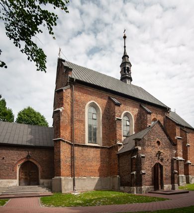Zdjęcie nr 41: Kościół jest zlokalizowany na wzgórzu, w centrum wsi. Murowany z cegły, w wątku polskim, z zendrówką. Kościół jest orientowany, założony na planie prostokąta, jednonawowy, trójprzęsłowy, z dobudowanymi kruchtami od zachodu i południa. Prezbiterium oddzielone od nawy łukiem tęczowym, dwuprzęsłowe na planie prostokąta, zamknięte prostą ścianą, z dwukondygnacyjną przybudówką zakończoną trójbocznie. Nawa została przykryta sklepieniem sieciowym. Ściana południowa nawy przepruta trzema prostokątnymi oknami, zamkniętymi łukiem ostrym. Okna w nawie i prezbiterium dwudzielne, z sześcioma mniejszymi kwaterami. Przybudówka przy prezbiterium na parterze mieści zakrystię, a na piętrze składzik. Kruchta południowa sklepiona kolebką. Z kruchty do nawy prowadzi ostrołukowy, kamienny portal o dwóch archiwoltach. Kruchta zachodnia, obecnie kaplica św. Franciszka, sklepiona spłaszczoną, ukrytą kopułą na pendentywach. Ściana zachodnia kruchty przepruta dwoma ostrołukowymi oknami i ponad nimi okrągłym oknem. Od południa ostrołukowe wejście. Kościół o zróżnicowanej wysokości nawy i prezbiterium. Ściany opięte szkarpami. Na jednej trzeciej wysokości ścian oraz w zwieńczeniu nawy i prezbiterium profilowany gzyms. Od zachodu wklęsło-wypukły szczyt. Nawa, prezbiterium i dwie kruchty przykryte dachem dwuspadowym. Nad drugim przęsłem prezbiterium wieżyczka na sygnaturkę na planie ośmioboku, z profilowanym gzymsem i latarnią, zwieńczoną hełmem z kulą i krzyżem. Wejście do kościoła od południa i zachodu. Okna nawy i prezbiterium z kamiennym obramieniem. Nad wejściem do kruchty południowej formowany w cegle ostry łuk. Analogiczny łuk nad oknami w ścianie zachodniej i nad blendą w ścianie północnej. W przybudówce do prezbiterium dwie kondygnacje okien zamkniętych łukiem ostrym. W ścianie frontowej prostokątne wejście, a nad nim półkoliście zamknięta wnęka z grupą Ukrzyżowania. 


