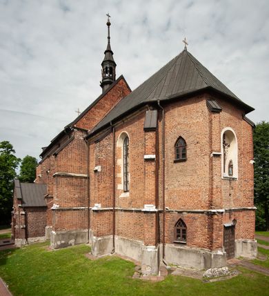Zdjęcie nr 17: Kościół jest zlokalizowany na wzgórzu, w centrum wsi. Murowany z cegły, w wątku polskim, z zendrówką. Kościół jest orientowany, założony na planie prostokąta, jednonawowy, trójprzęsłowy, z dobudowanymi kruchtami od zachodu i południa. Prezbiterium oddzielone od nawy łukiem tęczowym, dwuprzęsłowe na planie prostokąta, zamknięte prostą ścianą, z dwukondygnacyjną przybudówką zakończoną trójbocznie. Nawa została przykryta sklepieniem sieciowym. Ściana południowa nawy przepruta trzema prostokątnymi oknami, zamkniętymi łukiem ostrym. Okna w nawie i prezbiterium dwudzielne, z sześcioma mniejszymi kwaterami. Przybudówka przy prezbiterium na parterze mieści zakrystię, a na piętrze składzik. Kruchta południowa sklepiona kolebką. Z kruchty do nawy prowadzi ostrołukowy, kamienny portal o dwóch archiwoltach. Kruchta zachodnia, obecnie kaplica św. Franciszka, sklepiona spłaszczoną, ukrytą kopułą na pendentywach. Ściana zachodnia kruchty przepruta dwoma ostrołukowymi oknami i ponad nimi okrągłym oknem. Od południa ostrołukowe wejście. Kościół o zróżnicowanej wysokości nawy i prezbiterium. Ściany opięte szkarpami. Na jednej trzeciej wysokości ścian oraz w zwieńczeniu nawy i prezbiterium profilowany gzyms. Od zachodu wklęsło-wypukły szczyt. Nawa, prezbiterium i dwie kruchty przykryte dachem dwuspadowym. Nad drugim przęsłem prezbiterium wieżyczka na sygnaturkę na planie ośmioboku, z profilowanym gzymsem i latarnią, zwieńczoną hełmem z kulą i krzyżem. Wejście do kościoła od południa i zachodu. Okna nawy i prezbiterium z kamiennym obramieniem. Nad wejściem do kruchty południowej formowany w cegle ostry łuk. Analogiczny łuk nad oknami w ścianie zachodniej i nad blendą w ścianie północnej. W przybudówce do prezbiterium dwie kondygnacje okien zamkniętych łukiem ostrym. W ścianie frontowej prostokątne wejście, a nad nim półkoliście zamknięta wnęka z grupą Ukrzyżowania. 


