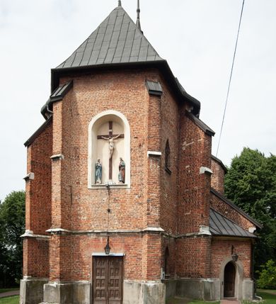 Zdjęcie nr 19: Kościół jest zlokalizowany na wzgórzu, w centrum wsi. Murowany z cegły, w wątku polskim, z zendrówką. Kościół jest orientowany, założony na planie prostokąta, jednonawowy, trójprzęsłowy, z dobudowanymi kruchtami od zachodu i południa. Prezbiterium oddzielone od nawy łukiem tęczowym, dwuprzęsłowe na planie prostokąta, zamknięte prostą ścianą, z dwukondygnacyjną przybudówką zakończoną trójbocznie. Nawa została przykryta sklepieniem sieciowym. Ściana południowa nawy przepruta trzema prostokątnymi oknami, zamkniętymi łukiem ostrym. Okna w nawie i prezbiterium dwudzielne, z sześcioma mniejszymi kwaterami. Przybudówka przy prezbiterium na parterze mieści zakrystię, a na piętrze składzik. Kruchta południowa sklepiona kolebką. Z kruchty do nawy prowadzi ostrołukowy, kamienny portal o dwóch archiwoltach. Kruchta zachodnia, obecnie kaplica św. Franciszka, sklepiona spłaszczoną, ukrytą kopułą na pendentywach. Ściana zachodnia kruchty przepruta dwoma ostrołukowymi oknami i ponad nimi okrągłym oknem. Od południa ostrołukowe wejście. Kościół o zróżnicowanej wysokości nawy i prezbiterium. Ściany opięte szkarpami. Na jednej trzeciej wysokości ścian oraz w zwieńczeniu nawy i prezbiterium profilowany gzyms. Od zachodu wklęsło-wypukły szczyt. Nawa, prezbiterium i dwie kruchty przykryte dachem dwuspadowym. Nad drugim przęsłem prezbiterium wieżyczka na sygnaturkę na planie ośmioboku, z profilowanym gzymsem i latarnią, zwieńczoną hełmem z kulą i krzyżem. Wejście do kościoła od południa i zachodu. Okna nawy i prezbiterium z kamiennym obramieniem. Nad wejściem do kruchty południowej formowany w cegle ostry łuk. Analogiczny łuk nad oknami w ścianie zachodniej i nad blendą w ścianie północnej. W przybudówce do prezbiterium dwie kondygnacje okien zamkniętych łukiem ostrym. W ścianie frontowej prostokątne wejście, a nad nim półkoliście zamknięta wnęka z grupą Ukrzyżowania. 


