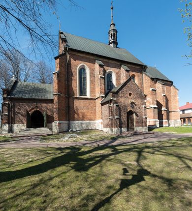 Zdjęcie nr 36: Kościół jest zlokalizowany na wzgórzu, w centrum wsi. Murowany z cegły, w wątku polskim, z zendrówką. Kościół jest orientowany, założony na planie prostokąta, jednonawowy, trójprzęsłowy, z dobudowanymi kruchtami od zachodu i południa. Prezbiterium oddzielone od nawy łukiem tęczowym, dwuprzęsłowe na planie prostokąta, zamknięte prostą ścianą, z dwukondygnacyjną przybudówką zakończoną trójbocznie. Nawa została przykryta sklepieniem sieciowym. Ściana południowa nawy przepruta trzema prostokątnymi oknami, zamkniętymi łukiem ostrym. Okna w nawie i prezbiterium dwudzielne, z sześcioma mniejszymi kwaterami. Przybudówka przy prezbiterium na parterze mieści zakrystię, a na piętrze składzik. Kruchta południowa sklepiona kolebką. Z kruchty do nawy prowadzi ostrołukowy, kamienny portal o dwóch archiwoltach. Kruchta zachodnia, obecnie kaplica św. Franciszka, sklepiona spłaszczoną, ukrytą kopułą na pendentywach. Ściana zachodnia kruchty przepruta dwoma ostrołukowymi oknami i ponad nimi okrągłym oknem. Od południa ostrołukowe wejście. Kościół o zróżnicowanej wysokości nawy i prezbiterium. Ściany opięte szkarpami. Na jednej trzeciej wysokości ścian oraz w zwieńczeniu nawy i prezbiterium profilowany gzyms. Od zachodu wklęsło-wypukły szczyt. Nawa, prezbiterium i dwie kruchty przykryte dachem dwuspadowym. Nad drugim przęsłem prezbiterium wieżyczka na sygnaturkę na planie ośmioboku, z profilowanym gzymsem i latarnią, zwieńczoną hełmem z kulą i krzyżem. Wejście do kościoła od południa i zachodu. Okna nawy i prezbiterium z kamiennym obramieniem. Nad wejściem do kruchty południowej formowany w cegle ostry łuk. Analogiczny łuk nad oknami w ścianie zachodniej i nad blendą w ścianie północnej. W przybudówce do prezbiterium dwie kondygnacje okien zamkniętych łukiem ostrym. W ścianie frontowej prostokątne wejście, a nad nim półkoliście zamknięta wnęka z grupą Ukrzyżowania. 


