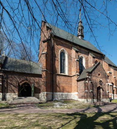 Zdjęcie nr 34: Kościół jest zlokalizowany na wzgórzu, w centrum wsi. Murowany z cegły, w wątku polskim, z zendrówką. Kościół jest orientowany, założony na planie prostokąta, jednonawowy, trójprzęsłowy, z dobudowanymi kruchtami od zachodu i południa. Prezbiterium oddzielone od nawy łukiem tęczowym, dwuprzęsłowe na planie prostokąta, zamknięte prostą ścianą, z dwukondygnacyjną przybudówką zakończoną trójbocznie. Nawa została przykryta sklepieniem sieciowym. Ściana południowa nawy przepruta trzema prostokątnymi oknami, zamkniętymi łukiem ostrym. Okna w nawie i prezbiterium dwudzielne, z sześcioma mniejszymi kwaterami. Przybudówka przy prezbiterium na parterze mieści zakrystię, a na piętrze składzik. Kruchta południowa sklepiona kolebką. Z kruchty do nawy prowadzi ostrołukowy, kamienny portal o dwóch archiwoltach. Kruchta zachodnia, obecnie kaplica św. Franciszka, sklepiona spłaszczoną, ukrytą kopułą na pendentywach. Ściana zachodnia kruchty przepruta dwoma ostrołukowymi oknami i ponad nimi okrągłym oknem. Od południa ostrołukowe wejście. Kościół o zróżnicowanej wysokości nawy i prezbiterium. Ściany opięte szkarpami. Na jednej trzeciej wysokości ścian oraz w zwieńczeniu nawy i prezbiterium profilowany gzyms. Od zachodu wklęsło-wypukły szczyt. Nawa, prezbiterium i dwie kruchty przykryte dachem dwuspadowym. Nad drugim przęsłem prezbiterium wieżyczka na sygnaturkę na planie ośmioboku, z profilowanym gzymsem i latarnią, zwieńczoną hełmem z kulą i krzyżem. Wejście do kościoła od południa i zachodu. Okna nawy i prezbiterium z kamiennym obramieniem. Nad wejściem do kruchty południowej formowany w cegle ostry łuk. Analogiczny łuk nad oknami w ścianie zachodniej i nad blendą w ścianie północnej. W przybudówce do prezbiterium dwie kondygnacje okien zamkniętych łukiem ostrym. W ścianie frontowej prostokątne wejście, a nad nim półkoliście zamknięta wnęka z grupą Ukrzyżowania. 


