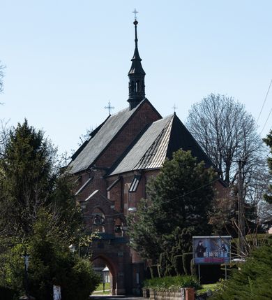 Zdjęcie nr 80: Kościół jest zlokalizowany na wzgórzu, w centrum wsi. Murowany z cegły, w wątku polskim, z zendrówką. Kościół jest orientowany, założony na planie prostokąta, jednonawowy, trójprzęsłowy, z dobudowanymi kruchtami od zachodu i południa. Prezbiterium oddzielone od nawy łukiem tęczowym, dwuprzęsłowe na planie prostokąta, zamknięte prostą ścianą, z dwukondygnacyjną przybudówką zakończoną trójbocznie. Nawa została przykryta sklepieniem sieciowym. Ściana południowa nawy przepruta trzema prostokątnymi oknami, zamkniętymi łukiem ostrym. Okna w nawie i prezbiterium dwudzielne, z sześcioma mniejszymi kwaterami. Przybudówka przy prezbiterium na parterze mieści zakrystię, a na piętrze składzik. Kruchta południowa sklepiona kolebką. Z kruchty do nawy prowadzi ostrołukowy, kamienny portal o dwóch archiwoltach. Kruchta zachodnia, obecnie kaplica św. Franciszka, sklepiona spłaszczoną, ukrytą kopułą na pendentywach. Ściana zachodnia kruchty przepruta dwoma ostrołukowymi oknami i ponad nimi okrągłym oknem. Od południa ostrołukowe wejście. Kościół o zróżnicowanej wysokości nawy i prezbiterium. Ściany opięte szkarpami. Na jednej trzeciej wysokości ścian oraz w zwieńczeniu nawy i prezbiterium profilowany gzyms. Od zachodu wklęsło-wypukły szczyt. Nawa, prezbiterium i dwie kruchty przykryte dachem dwuspadowym. Nad drugim przęsłem prezbiterium wieżyczka na sygnaturkę na planie ośmioboku, z profilowanym gzymsem i latarnią, zwieńczoną hełmem z kulą i krzyżem. Wejście do kościoła od południa i zachodu. Okna nawy i prezbiterium z kamiennym obramieniem. Nad wejściem do kruchty południowej formowany w cegle ostry łuk. Analogiczny łuk nad oknami w ścianie zachodniej i nad blendą w ścianie północnej. W przybudówce do prezbiterium dwie kondygnacje okien zamkniętych łukiem ostrym. W ścianie frontowej prostokątne wejście, a nad nim półkoliście zamknięta wnęka z grupą Ukrzyżowania. 


