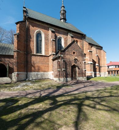 Zdjęcie nr 37: Kościół jest zlokalizowany na wzgórzu, w centrum wsi. Murowany z cegły, w wątku polskim, z zendrówką. Kościół jest orientowany, założony na planie prostokąta, jednonawowy, trójprzęsłowy, z dobudowanymi kruchtami od zachodu i południa. Prezbiterium oddzielone od nawy łukiem tęczowym, dwuprzęsłowe na planie prostokąta, zamknięte prostą ścianą, z dwukondygnacyjną przybudówką zakończoną trójbocznie. Nawa została przykryta sklepieniem sieciowym. Ściana południowa nawy przepruta trzema prostokątnymi oknami, zamkniętymi łukiem ostrym. Okna w nawie i prezbiterium dwudzielne, z sześcioma mniejszymi kwaterami. Przybudówka przy prezbiterium na parterze mieści zakrystię, a na piętrze składzik. Kruchta południowa sklepiona kolebką. Z kruchty do nawy prowadzi ostrołukowy, kamienny portal o dwóch archiwoltach. Kruchta zachodnia, obecnie kaplica św. Franciszka, sklepiona spłaszczoną, ukrytą kopułą na pendentywach. Ściana zachodnia kruchty przepruta dwoma ostrołukowymi oknami i ponad nimi okrągłym oknem. Od południa ostrołukowe wejście. Kościół o zróżnicowanej wysokości nawy i prezbiterium. Ściany opięte szkarpami. Na jednej trzeciej wysokości ścian oraz w zwieńczeniu nawy i prezbiterium profilowany gzyms. Od zachodu wklęsło-wypukły szczyt. Nawa, prezbiterium i dwie kruchty przykryte dachem dwuspadowym. Nad drugim przęsłem prezbiterium wieżyczka na sygnaturkę na planie ośmioboku, z profilowanym gzymsem i latarnią, zwieńczoną hełmem z kulą i krzyżem. Wejście do kościoła od południa i zachodu. Okna nawy i prezbiterium z kamiennym obramieniem. Nad wejściem do kruchty południowej formowany w cegle ostry łuk. Analogiczny łuk nad oknami w ścianie zachodniej i nad blendą w ścianie północnej. W przybudówce do prezbiterium dwie kondygnacje okien zamkniętych łukiem ostrym. W ścianie frontowej prostokątne wejście, a nad nim półkoliście zamknięta wnęka z grupą Ukrzyżowania. 


