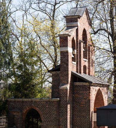 Zdjęcie nr 14: Kościół jest zlokalizowany na wzgórzu, w centrum wsi. Murowany z cegły, w wątku polskim, z zendrówką. Kościół jest orientowany, założony na planie prostokąta, jednonawowy, trójprzęsłowy, z dobudowanymi kruchtami od zachodu i południa. Prezbiterium oddzielone od nawy łukiem tęczowym, dwuprzęsłowe na planie prostokąta, zamknięte prostą ścianą, z dwukondygnacyjną przybudówką zakończoną trójbocznie. Nawa została przykryta sklepieniem sieciowym. Ściana południowa nawy przepruta trzema prostokątnymi oknami, zamkniętymi łukiem ostrym. Okna w nawie i prezbiterium dwudzielne, z sześcioma mniejszymi kwaterami. Przybudówka przy prezbiterium na parterze mieści zakrystię, a na piętrze składzik. Kruchta południowa sklepiona kolebką. Z kruchty do nawy prowadzi ostrołukowy, kamienny portal o dwóch archiwoltach. Kruchta zachodnia, obecnie kaplica św. Franciszka, sklepiona spłaszczoną, ukrytą kopułą na pendentywach. Ściana zachodnia kruchty przepruta dwoma ostrołukowymi oknami i ponad nimi okrągłym oknem. Od południa ostrołukowe wejście. Kościół o zróżnicowanej wysokości nawy i prezbiterium. Ściany opięte szkarpami. Na jednej trzeciej wysokości ścian oraz w zwieńczeniu nawy i prezbiterium profilowany gzyms. Od zachodu wklęsło-wypukły szczyt. Nawa, prezbiterium i dwie kruchty przykryte dachem dwuspadowym. Nad drugim przęsłem prezbiterium wieżyczka na sygnaturkę na planie ośmioboku, z profilowanym gzymsem i latarnią, zwieńczoną hełmem z kulą i krzyżem. Wejście do kościoła od południa i zachodu. Okna nawy i prezbiterium z kamiennym obramieniem. Nad wejściem do kruchty południowej formowany w cegle ostry łuk. Analogiczny łuk nad oknami w ścianie zachodniej i nad blendą w ścianie północnej. W przybudówce do prezbiterium dwie kondygnacje okien zamkniętych łukiem ostrym. W ścianie frontowej prostokątne wejście, a nad nim półkoliście zamknięta wnęka z grupą Ukrzyżowania. 


