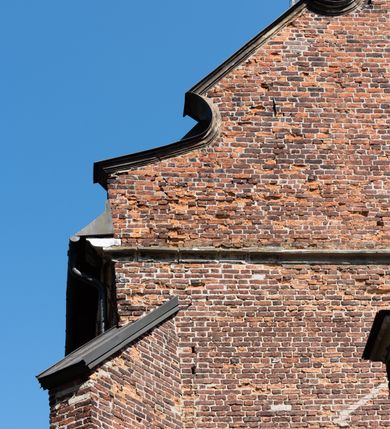 Zdjęcie nr 64: Kościół jest zlokalizowany na wzgórzu, w centrum wsi. Murowany z cegły, w wątku polskim, z zendrówką. Kościół jest orientowany, założony na planie prostokąta, jednonawowy, trójprzęsłowy, z dobudowanymi kruchtami od zachodu i południa. Prezbiterium oddzielone od nawy łukiem tęczowym, dwuprzęsłowe na planie prostokąta, zamknięte prostą ścianą, z dwukondygnacyjną przybudówką zakończoną trójbocznie. Nawa została przykryta sklepieniem sieciowym. Ściana południowa nawy przepruta trzema prostokątnymi oknami, zamkniętymi łukiem ostrym. Okna w nawie i prezbiterium dwudzielne, z sześcioma mniejszymi kwaterami. Przybudówka przy prezbiterium na parterze mieści zakrystię, a na piętrze składzik. Kruchta południowa sklepiona kolebką. Z kruchty do nawy prowadzi ostrołukowy, kamienny portal o dwóch archiwoltach. Kruchta zachodnia, obecnie kaplica św. Franciszka, sklepiona spłaszczoną, ukrytą kopułą na pendentywach. Ściana zachodnia kruchty przepruta dwoma ostrołukowymi oknami i ponad nimi okrągłym oknem. Od południa ostrołukowe wejście. Kościół o zróżnicowanej wysokości nawy i prezbiterium. Ściany opięte szkarpami. Na jednej trzeciej wysokości ścian oraz w zwieńczeniu nawy i prezbiterium profilowany gzyms. Od zachodu wklęsło-wypukły szczyt. Nawa, prezbiterium i dwie kruchty przykryte dachem dwuspadowym. Nad drugim przęsłem prezbiterium wieżyczka na sygnaturkę na planie ośmioboku, z profilowanym gzymsem i latarnią, zwieńczoną hełmem z kulą i krzyżem. Wejście do kościoła od południa i zachodu. Okna nawy i prezbiterium z kamiennym obramieniem. Nad wejściem do kruchty południowej formowany w cegle ostry łuk. Analogiczny łuk nad oknami w ścianie zachodniej i nad blendą w ścianie północnej. W przybudówce do prezbiterium dwie kondygnacje okien zamkniętych łukiem ostrym. W ścianie frontowej prostokątne wejście, a nad nim półkoliście zamknięta wnęka z grupą Ukrzyżowania. 


