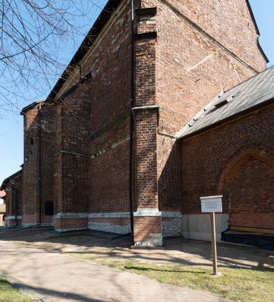 Zdjęcie nr 55: Kościół jest zlokalizowany na wzgórzu, w centrum wsi. Murowany z cegły, w wątku polskim, z zendrówką. Kościół jest orientowany, założony na planie prostokąta, jednonawowy, trójprzęsłowy, z dobudowanymi kruchtami od zachodu i południa. Prezbiterium oddzielone od nawy łukiem tęczowym, dwuprzęsłowe na planie prostokąta, zamknięte prostą ścianą, z dwukondygnacyjną przybudówką zakończoną trójbocznie. Nawa została przykryta sklepieniem sieciowym. Ściana południowa nawy przepruta trzema prostokątnymi oknami, zamkniętymi łukiem ostrym. Okna w nawie i prezbiterium dwudzielne, z sześcioma mniejszymi kwaterami. Przybudówka przy prezbiterium na parterze mieści zakrystię, a na piętrze składzik. Kruchta południowa sklepiona kolebką. Z kruchty do nawy prowadzi ostrołukowy, kamienny portal o dwóch archiwoltach. Kruchta zachodnia, obecnie kaplica św. Franciszka, sklepiona spłaszczoną, ukrytą kopułą na pendentywach. Ściana zachodnia kruchty przepruta dwoma ostrołukowymi oknami i ponad nimi okrągłym oknem. Od południa ostrołukowe wejście. Kościół o zróżnicowanej wysokości nawy i prezbiterium. Ściany opięte szkarpami. Na jednej trzeciej wysokości ścian oraz w zwieńczeniu nawy i prezbiterium profilowany gzyms. Od zachodu wklęsło-wypukły szczyt. Nawa, prezbiterium i dwie kruchty przykryte dachem dwuspadowym. Nad drugim przęsłem prezbiterium wieżyczka na sygnaturkę na planie ośmioboku, z profilowanym gzymsem i latarnią, zwieńczoną hełmem z kulą i krzyżem. Wejście do kościoła od południa i zachodu. Okna nawy i prezbiterium z kamiennym obramieniem. Nad wejściem do kruchty południowej formowany w cegle ostry łuk. Analogiczny łuk nad oknami w ścianie zachodniej i nad blendą w ścianie północnej. W przybudówce do prezbiterium dwie kondygnacje okien zamkniętych łukiem ostrym. W ścianie frontowej prostokątne wejście, a nad nim półkoliście zamknięta wnęka z grupą Ukrzyżowania. 


