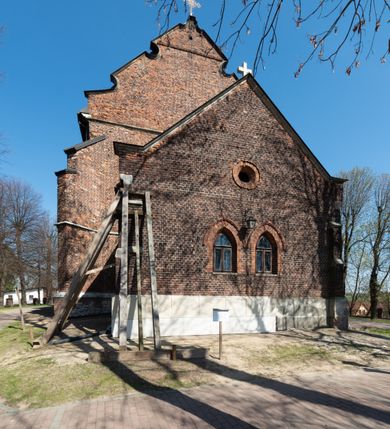 Zdjęcie nr 53: Kościół jest zlokalizowany na wzgórzu, w centrum wsi. Murowany z cegły, w wątku polskim, z zendrówką. Kościół jest orientowany, założony na planie prostokąta, jednonawowy, trójprzęsłowy, z dobudowanymi kruchtami od zachodu i południa. Prezbiterium oddzielone od nawy łukiem tęczowym, dwuprzęsłowe na planie prostokąta, zamknięte prostą ścianą, z dwukondygnacyjną przybudówką zakończoną trójbocznie. Nawa została przykryta sklepieniem sieciowym. Ściana południowa nawy przepruta trzema prostokątnymi oknami, zamkniętymi łukiem ostrym. Okna w nawie i prezbiterium dwudzielne, z sześcioma mniejszymi kwaterami. Przybudówka przy prezbiterium na parterze mieści zakrystię, a na piętrze składzik. Kruchta południowa sklepiona kolebką. Z kruchty do nawy prowadzi ostrołukowy, kamienny portal o dwóch archiwoltach. Kruchta zachodnia, obecnie kaplica św. Franciszka, sklepiona spłaszczoną, ukrytą kopułą na pendentywach. Ściana zachodnia kruchty przepruta dwoma ostrołukowymi oknami i ponad nimi okrągłym oknem. Od południa ostrołukowe wejście. Kościół o zróżnicowanej wysokości nawy i prezbiterium. Ściany opięte szkarpami. Na jednej trzeciej wysokości ścian oraz w zwieńczeniu nawy i prezbiterium profilowany gzyms. Od zachodu wklęsło-wypukły szczyt. Nawa, prezbiterium i dwie kruchty przykryte dachem dwuspadowym. Nad drugim przęsłem prezbiterium wieżyczka na sygnaturkę na planie ośmioboku, z profilowanym gzymsem i latarnią, zwieńczoną hełmem z kulą i krzyżem. Wejście do kościoła od południa i zachodu. Okna nawy i prezbiterium z kamiennym obramieniem. Nad wejściem do kruchty południowej formowany w cegle ostry łuk. Analogiczny łuk nad oknami w ścianie zachodniej i nad blendą w ścianie północnej. W przybudówce do prezbiterium dwie kondygnacje okien zamkniętych łukiem ostrym. W ścianie frontowej prostokątne wejście, a nad nim półkoliście zamknięta wnęka z grupą Ukrzyżowania. 


