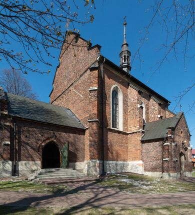 Zdjęcie nr 39: Kościół jest zlokalizowany na wzgórzu, w centrum wsi. Murowany z cegły, w wątku polskim, z zendrówką. Kościół jest orientowany, założony na planie prostokąta, jednonawowy, trójprzęsłowy, z dobudowanymi kruchtami od zachodu i południa. Prezbiterium oddzielone od nawy łukiem tęczowym, dwuprzęsłowe na planie prostokąta, zamknięte prostą ścianą, z dwukondygnacyjną przybudówką zakończoną trójbocznie. Nawa została przykryta sklepieniem sieciowym. Ściana południowa nawy przepruta trzema prostokątnymi oknami, zamkniętymi łukiem ostrym. Okna w nawie i prezbiterium dwudzielne, z sześcioma mniejszymi kwaterami. Przybudówka przy prezbiterium na parterze mieści zakrystię, a na piętrze składzik. Kruchta południowa sklepiona kolebką. Z kruchty do nawy prowadzi ostrołukowy, kamienny portal o dwóch archiwoltach. Kruchta zachodnia, obecnie kaplica św. Franciszka, sklepiona spłaszczoną, ukrytą kopułą na pendentywach. Ściana zachodnia kruchty przepruta dwoma ostrołukowymi oknami i ponad nimi okrągłym oknem. Od południa ostrołukowe wejście. Kościół o zróżnicowanej wysokości nawy i prezbiterium. Ściany opięte szkarpami. Na jednej trzeciej wysokości ścian oraz w zwieńczeniu nawy i prezbiterium profilowany gzyms. Od zachodu wklęsło-wypukły szczyt. Nawa, prezbiterium i dwie kruchty przykryte dachem dwuspadowym. Nad drugim przęsłem prezbiterium wieżyczka na sygnaturkę na planie ośmioboku, z profilowanym gzymsem i latarnią, zwieńczoną hełmem z kulą i krzyżem. Wejście do kościoła od południa i zachodu. Okna nawy i prezbiterium z kamiennym obramieniem. Nad wejściem do kruchty południowej formowany w cegle ostry łuk. Analogiczny łuk nad oknami w ścianie zachodniej i nad blendą w ścianie północnej. W przybudówce do prezbiterium dwie kondygnacje okien zamkniętych łukiem ostrym. W ścianie frontowej prostokątne wejście, a nad nim półkoliście zamknięta wnęka z grupą Ukrzyżowania. 


