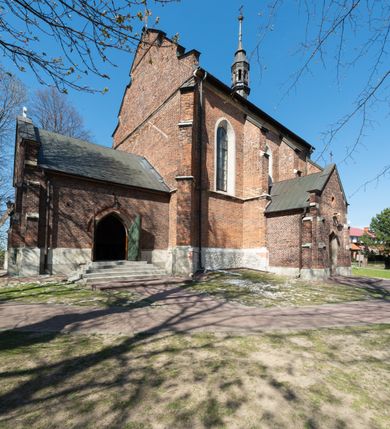 Zdjęcie nr 38: Kościół jest zlokalizowany na wzgórzu, w centrum wsi. Murowany z cegły, w wątku polskim, z zendrówką. Kościół jest orientowany, założony na planie prostokąta, jednonawowy, trójprzęsłowy, z dobudowanymi kruchtami od zachodu i południa. Prezbiterium oddzielone od nawy łukiem tęczowym, dwuprzęsłowe na planie prostokąta, zamknięte prostą ścianą, z dwukondygnacyjną przybudówką zakończoną trójbocznie. Nawa została przykryta sklepieniem sieciowym. Ściana południowa nawy przepruta trzema prostokątnymi oknami, zamkniętymi łukiem ostrym. Okna w nawie i prezbiterium dwudzielne, z sześcioma mniejszymi kwaterami. Przybudówka przy prezbiterium na parterze mieści zakrystię, a na piętrze składzik. Kruchta południowa sklepiona kolebką. Z kruchty do nawy prowadzi ostrołukowy, kamienny portal o dwóch archiwoltach. Kruchta zachodnia, obecnie kaplica św. Franciszka, sklepiona spłaszczoną, ukrytą kopułą na pendentywach. Ściana zachodnia kruchty przepruta dwoma ostrołukowymi oknami i ponad nimi okrągłym oknem. Od południa ostrołukowe wejście. Kościół o zróżnicowanej wysokości nawy i prezbiterium. Ściany opięte szkarpami. Na jednej trzeciej wysokości ścian oraz w zwieńczeniu nawy i prezbiterium profilowany gzyms. Od zachodu wklęsło-wypukły szczyt. Nawa, prezbiterium i dwie kruchty przykryte dachem dwuspadowym. Nad drugim przęsłem prezbiterium wieżyczka na sygnaturkę na planie ośmioboku, z profilowanym gzymsem i latarnią, zwieńczoną hełmem z kulą i krzyżem. Wejście do kościoła od południa i zachodu. Okna nawy i prezbiterium z kamiennym obramieniem. Nad wejściem do kruchty południowej formowany w cegle ostry łuk. Analogiczny łuk nad oknami w ścianie zachodniej i nad blendą w ścianie północnej. W przybudówce do prezbiterium dwie kondygnacje okien zamkniętych łukiem ostrym. W ścianie frontowej prostokątne wejście, a nad nim półkoliście zamknięta wnęka z grupą Ukrzyżowania. 


