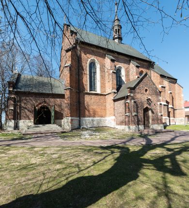 Zdjęcie nr 35: Kościół jest zlokalizowany na wzgórzu, w centrum wsi. Murowany z cegły, w wątku polskim, z zendrówką. Kościół jest orientowany, założony na planie prostokąta, jednonawowy, trójprzęsłowy, z dobudowanymi kruchtami od zachodu i południa. Prezbiterium oddzielone od nawy łukiem tęczowym, dwuprzęsłowe na planie prostokąta, zamknięte prostą ścianą, z dwukondygnacyjną przybudówką zakończoną trójbocznie. Nawa została przykryta sklepieniem sieciowym. Ściana południowa nawy przepruta trzema prostokątnymi oknami, zamkniętymi łukiem ostrym. Okna w nawie i prezbiterium dwudzielne, z sześcioma mniejszymi kwaterami. Przybudówka przy prezbiterium na parterze mieści zakrystię, a na piętrze składzik. Kruchta południowa sklepiona kolebką. Z kruchty do nawy prowadzi ostrołukowy, kamienny portal o dwóch archiwoltach. Kruchta zachodnia, obecnie kaplica św. Franciszka, sklepiona spłaszczoną, ukrytą kopułą na pendentywach. Ściana zachodnia kruchty przepruta dwoma ostrołukowymi oknami i ponad nimi okrągłym oknem. Od południa ostrołukowe wejście. Kościół o zróżnicowanej wysokości nawy i prezbiterium. Ściany opięte szkarpami. Na jednej trzeciej wysokości ścian oraz w zwieńczeniu nawy i prezbiterium profilowany gzyms. Od zachodu wklęsło-wypukły szczyt. Nawa, prezbiterium i dwie kruchty przykryte dachem dwuspadowym. Nad drugim przęsłem prezbiterium wieżyczka na sygnaturkę na planie ośmioboku, z profilowanym gzymsem i latarnią, zwieńczoną hełmem z kulą i krzyżem. Wejście do kościoła od południa i zachodu. Okna nawy i prezbiterium z kamiennym obramieniem. Nad wejściem do kruchty południowej formowany w cegle ostry łuk. Analogiczny łuk nad oknami w ścianie zachodniej i nad blendą w ścianie północnej. W przybudówce do prezbiterium dwie kondygnacje okien zamkniętych łukiem ostrym. W ścianie frontowej prostokątne wejście, a nad nim półkoliście zamknięta wnęka z grupą Ukrzyżowania. 


