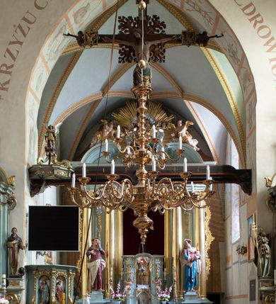 Zdjęcie nr 90: Kościół jest zlokalizowany na wzgórzu, w centrum wsi. Murowany z cegły, w wątku polskim, z zendrówką. Kościół jest orientowany, założony na planie prostokąta, jednonawowy, trójprzęsłowy, z dobudowanymi kruchtami od zachodu i południa. Prezbiterium oddzielone od nawy łukiem tęczowym, dwuprzęsłowe na planie prostokąta, zamknięte prostą ścianą, z dwukondygnacyjną przybudówką zakończoną trójbocznie. Nawa została przykryta sklepieniem sieciowym. Ściana południowa nawy przepruta trzema prostokątnymi oknami, zamkniętymi łukiem ostrym. Okna w nawie i prezbiterium dwudzielne, z sześcioma mniejszymi kwaterami. Przybudówka przy prezbiterium na parterze mieści zakrystię, a na piętrze składzik. Kruchta południowa sklepiona kolebką. Z kruchty do nawy prowadzi ostrołukowy, kamienny portal o dwóch archiwoltach. Kruchta zachodnia, obecnie kaplica św. Franciszka, sklepiona spłaszczoną, ukrytą kopułą na pendentywach. Ściana zachodnia kruchty przepruta dwoma ostrołukowymi oknami i ponad nimi okrągłym oknem. Od południa ostrołukowe wejście. Kościół o zróżnicowanej wysokości nawy i prezbiterium. Ściany opięte szkarpami. Na jednej trzeciej wysokości ścian oraz w zwieńczeniu nawy i prezbiterium profilowany gzyms. Od zachodu wklęsło-wypukły szczyt. Nawa, prezbiterium i dwie kruchty przykryte dachem dwuspadowym. Nad drugim przęsłem prezbiterium wieżyczka na sygnaturkę na planie ośmioboku, z profilowanym gzymsem i latarnią, zwieńczoną hełmem z kulą i krzyżem. Wejście do kościoła od południa i zachodu. Okna nawy i prezbiterium z kamiennym obramieniem. Nad wejściem do kruchty południowej formowany w cegle ostry łuk. Analogiczny łuk nad oknami w ścianie zachodniej i nad blendą w ścianie północnej. W przybudówce do prezbiterium dwie kondygnacje okien zamkniętych łukiem ostrym. W ścianie frontowej prostokątne wejście, a nad nim półkoliście zamknięta wnęka z grupą Ukrzyżowania. 


