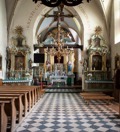 Zdjęcie nr 87: Kościół jest zlokalizowany na wzgórzu, w centrum wsi. Murowany z cegły, w wątku polskim, z zendrówką. Kościół jest orientowany, założony na planie prostokąta, jednonawowy, trójprzęsłowy, z dobudowanymi kruchtami od zachodu i południa. Prezbiterium oddzielone od nawy łukiem tęczowym, dwuprzęsłowe na planie prostokąta, zamknięte prostą ścianą, z dwukondygnacyjną przybudówką zakończoną trójbocznie. Nawa została przykryta sklepieniem sieciowym. Ściana południowa nawy przepruta trzema prostokątnymi oknami, zamkniętymi łukiem ostrym. Okna w nawie i prezbiterium dwudzielne, z sześcioma mniejszymi kwaterami. Przybudówka przy prezbiterium na parterze mieści zakrystię, a na piętrze składzik. Kruchta południowa sklepiona kolebką. Z kruchty do nawy prowadzi ostrołukowy, kamienny portal o dwóch archiwoltach. Kruchta zachodnia, obecnie kaplica św. Franciszka, sklepiona spłaszczoną, ukrytą kopułą na pendentywach. Ściana zachodnia kruchty przepruta dwoma ostrołukowymi oknami i ponad nimi okrągłym oknem. Od południa ostrołukowe wejście. Kościół o zróżnicowanej wysokości nawy i prezbiterium. Ściany opięte szkarpami. Na jednej trzeciej wysokości ścian oraz w zwieńczeniu nawy i prezbiterium profilowany gzyms. Od zachodu wklęsło-wypukły szczyt. Nawa, prezbiterium i dwie kruchty przykryte dachem dwuspadowym. Nad drugim przęsłem prezbiterium wieżyczka na sygnaturkę na planie ośmioboku, z profilowanym gzymsem i latarnią, zwieńczoną hełmem z kulą i krzyżem. Wejście do kościoła od południa i zachodu. Okna nawy i prezbiterium z kamiennym obramieniem. Nad wejściem do kruchty południowej formowany w cegle ostry łuk. Analogiczny łuk nad oknami w ścianie zachodniej i nad blendą w ścianie północnej. W przybudówce do prezbiterium dwie kondygnacje okien zamkniętych łukiem ostrym. W ścianie frontowej prostokątne wejście, a nad nim półkoliście zamknięta wnęka z grupą Ukrzyżowania. 


