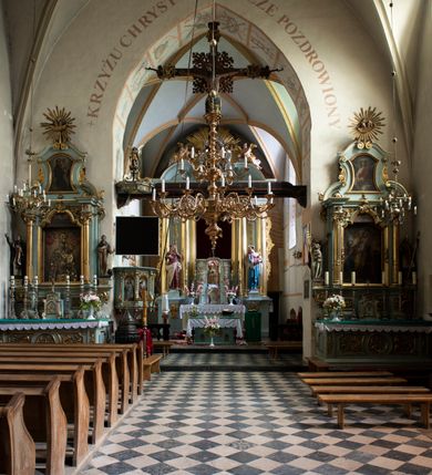Zdjęcie nr 88: Kościół jest zlokalizowany na wzgórzu, w centrum wsi. Murowany z cegły, w wątku polskim, z zendrówką. Kościół jest orientowany, założony na planie prostokąta, jednonawowy, trójprzęsłowy, z dobudowanymi kruchtami od zachodu i południa. Prezbiterium oddzielone od nawy łukiem tęczowym, dwuprzęsłowe na planie prostokąta, zamknięte prostą ścianą, z dwukondygnacyjną przybudówką zakończoną trójbocznie. Nawa została przykryta sklepieniem sieciowym. Ściana południowa nawy przepruta trzema prostokątnymi oknami, zamkniętymi łukiem ostrym. Okna w nawie i prezbiterium dwudzielne, z sześcioma mniejszymi kwaterami. Przybudówka przy prezbiterium na parterze mieści zakrystię, a na piętrze składzik. Kruchta południowa sklepiona kolebką. Z kruchty do nawy prowadzi ostrołukowy, kamienny portal o dwóch archiwoltach. Kruchta zachodnia, obecnie kaplica św. Franciszka, sklepiona spłaszczoną, ukrytą kopułą na pendentywach. Ściana zachodnia kruchty przepruta dwoma ostrołukowymi oknami i ponad nimi okrągłym oknem. Od południa ostrołukowe wejście. Kościół o zróżnicowanej wysokości nawy i prezbiterium. Ściany opięte szkarpami. Na jednej trzeciej wysokości ścian oraz w zwieńczeniu nawy i prezbiterium profilowany gzyms. Od zachodu wklęsło-wypukły szczyt. Nawa, prezbiterium i dwie kruchty przykryte dachem dwuspadowym. Nad drugim przęsłem prezbiterium wieżyczka na sygnaturkę na planie ośmioboku, z profilowanym gzymsem i latarnią, zwieńczoną hełmem z kulą i krzyżem. Wejście do kościoła od południa i zachodu. Okna nawy i prezbiterium z kamiennym obramieniem. Nad wejściem do kruchty południowej formowany w cegle ostry łuk. Analogiczny łuk nad oknami w ścianie zachodniej i nad blendą w ścianie północnej. W przybudówce do prezbiterium dwie kondygnacje okien zamkniętych łukiem ostrym. W ścianie frontowej prostokątne wejście, a nad nim półkoliście zamknięta wnęka z grupą Ukrzyżowania. 


