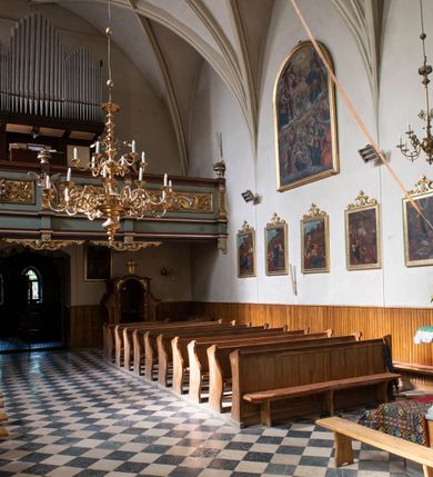 Zdjęcie nr 93: Kościół jest zlokalizowany na wzgórzu, w centrum wsi. Murowany z cegły, w wątku polskim, z zendrówką. Kościół jest orientowany, założony na planie prostokąta, jednonawowy, trójprzęsłowy, z dobudowanymi kruchtami od zachodu i południa. Prezbiterium oddzielone od nawy łukiem tęczowym, dwuprzęsłowe na planie prostokąta, zamknięte prostą ścianą, z dwukondygnacyjną przybudówką zakończoną trójbocznie. Nawa została przykryta sklepieniem sieciowym. Ściana południowa nawy przepruta trzema prostokątnymi oknami, zamkniętymi łukiem ostrym. Okna w nawie i prezbiterium dwudzielne, z sześcioma mniejszymi kwaterami. Przybudówka przy prezbiterium na parterze mieści zakrystię, a na piętrze składzik. Kruchta południowa sklepiona kolebką. Z kruchty do nawy prowadzi ostrołukowy, kamienny portal o dwóch archiwoltach. Kruchta zachodnia, obecnie kaplica św. Franciszka, sklepiona spłaszczoną, ukrytą kopułą na pendentywach. Ściana zachodnia kruchty przepruta dwoma ostrołukowymi oknami i ponad nimi okrągłym oknem. Od południa ostrołukowe wejście. Kościół o zróżnicowanej wysokości nawy i prezbiterium. Ściany opięte szkarpami. Na jednej trzeciej wysokości ścian oraz w zwieńczeniu nawy i prezbiterium profilowany gzyms. Od zachodu wklęsło-wypukły szczyt. Nawa, prezbiterium i dwie kruchty przykryte dachem dwuspadowym. Nad drugim przęsłem prezbiterium wieżyczka na sygnaturkę na planie ośmioboku, z profilowanym gzymsem i latarnią, zwieńczoną hełmem z kulą i krzyżem. Wejście do kościoła od południa i zachodu. Okna nawy i prezbiterium z kamiennym obramieniem. Nad wejściem do kruchty południowej formowany w cegle ostry łuk. Analogiczny łuk nad oknami w ścianie zachodniej i nad blendą w ścianie północnej. W przybudówce do prezbiterium dwie kondygnacje okien zamkniętych łukiem ostrym. W ścianie frontowej prostokątne wejście, a nad nim półkoliście zamknięta wnęka z grupą Ukrzyżowania. 


