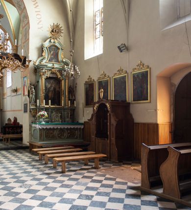 Zdjęcie nr 91: Kościół jest zlokalizowany na wzgórzu, w centrum wsi. Murowany z cegły, w wątku polskim, z zendrówką. Kościół jest orientowany, założony na planie prostokąta, jednonawowy, trójprzęsłowy, z dobudowanymi kruchtami od zachodu i południa. Prezbiterium oddzielone od nawy łukiem tęczowym, dwuprzęsłowe na planie prostokąta, zamknięte prostą ścianą, z dwukondygnacyjną przybudówką zakończoną trójbocznie. Nawa została przykryta sklepieniem sieciowym. Ściana południowa nawy przepruta trzema prostokątnymi oknami, zamkniętymi łukiem ostrym. Okna w nawie i prezbiterium dwudzielne, z sześcioma mniejszymi kwaterami. Przybudówka przy prezbiterium na parterze mieści zakrystię, a na piętrze składzik. Kruchta południowa sklepiona kolebką. Z kruchty do nawy prowadzi ostrołukowy, kamienny portal o dwóch archiwoltach. Kruchta zachodnia, obecnie kaplica św. Franciszka, sklepiona spłaszczoną, ukrytą kopułą na pendentywach. Ściana zachodnia kruchty przepruta dwoma ostrołukowymi oknami i ponad nimi okrągłym oknem. Od południa ostrołukowe wejście. Kościół o zróżnicowanej wysokości nawy i prezbiterium. Ściany opięte szkarpami. Na jednej trzeciej wysokości ścian oraz w zwieńczeniu nawy i prezbiterium profilowany gzyms. Od zachodu wklęsło-wypukły szczyt. Nawa, prezbiterium i dwie kruchty przykryte dachem dwuspadowym. Nad drugim przęsłem prezbiterium wieżyczka na sygnaturkę na planie ośmioboku, z profilowanym gzymsem i latarnią, zwieńczoną hełmem z kulą i krzyżem. Wejście do kościoła od południa i zachodu. Okna nawy i prezbiterium z kamiennym obramieniem. Nad wejściem do kruchty południowej formowany w cegle ostry łuk. Analogiczny łuk nad oknami w ścianie zachodniej i nad blendą w ścianie północnej. W przybudówce do prezbiterium dwie kondygnacje okien zamkniętych łukiem ostrym. W ścianie frontowej prostokątne wejście, a nad nim półkoliście zamknięta wnęka z grupą Ukrzyżowania. 


