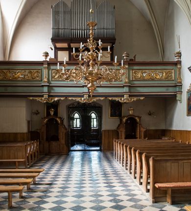 Zdjęcie nr 95: Kościół jest zlokalizowany na wzgórzu, w centrum wsi. Murowany z cegły, w wątku polskim, z zendrówką. Kościół jest orientowany, założony na planie prostokąta, jednonawowy, trójprzęsłowy, z dobudowanymi kruchtami od zachodu i południa. Prezbiterium oddzielone od nawy łukiem tęczowym, dwuprzęsłowe na planie prostokąta, zamknięte prostą ścianą, z dwukondygnacyjną przybudówką zakończoną trójbocznie. Nawa została przykryta sklepieniem sieciowym. Ściana południowa nawy przepruta trzema prostokątnymi oknami, zamkniętymi łukiem ostrym. Okna w nawie i prezbiterium dwudzielne, z sześcioma mniejszymi kwaterami. Przybudówka przy prezbiterium na parterze mieści zakrystię, a na piętrze składzik. Kruchta południowa sklepiona kolebką. Z kruchty do nawy prowadzi ostrołukowy, kamienny portal o dwóch archiwoltach. Kruchta zachodnia, obecnie kaplica św. Franciszka, sklepiona spłaszczoną, ukrytą kopułą na pendentywach. Ściana zachodnia kruchty przepruta dwoma ostrołukowymi oknami i ponad nimi okrągłym oknem. Od południa ostrołukowe wejście. Kościół o zróżnicowanej wysokości nawy i prezbiterium. Ściany opięte szkarpami. Na jednej trzeciej wysokości ścian oraz w zwieńczeniu nawy i prezbiterium profilowany gzyms. Od zachodu wklęsło-wypukły szczyt. Nawa, prezbiterium i dwie kruchty przykryte dachem dwuspadowym. Nad drugim przęsłem prezbiterium wieżyczka na sygnaturkę na planie ośmioboku, z profilowanym gzymsem i latarnią, zwieńczoną hełmem z kulą i krzyżem. Wejście do kościoła od południa i zachodu. Okna nawy i prezbiterium z kamiennym obramieniem. Nad wejściem do kruchty południowej formowany w cegle ostry łuk. Analogiczny łuk nad oknami w ścianie zachodniej i nad blendą w ścianie północnej. W przybudówce do prezbiterium dwie kondygnacje okien zamkniętych łukiem ostrym. W ścianie frontowej prostokątne wejście, a nad nim półkoliście zamknięta wnęka z grupą Ukrzyżowania. 


