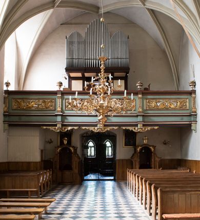 Zdjęcie nr 98: Kościół jest zlokalizowany na wzgórzu, w centrum wsi. Murowany z cegły, w wątku polskim, z zendrówką. Kościół jest orientowany, założony na planie prostokąta, jednonawowy, trójprzęsłowy, z dobudowanymi kruchtami od zachodu i południa. Prezbiterium oddzielone od nawy łukiem tęczowym, dwuprzęsłowe na planie prostokąta, zamknięte prostą ścianą, z dwukondygnacyjną przybudówką zakończoną trójbocznie. Nawa została przykryta sklepieniem sieciowym. Ściana południowa nawy przepruta trzema prostokątnymi oknami, zamkniętymi łukiem ostrym. Okna w nawie i prezbiterium dwudzielne, z sześcioma mniejszymi kwaterami. Przybudówka przy prezbiterium na parterze mieści zakrystię, a na piętrze składzik. Kruchta południowa sklepiona kolebką. Z kruchty do nawy prowadzi ostrołukowy, kamienny portal o dwóch archiwoltach. Kruchta zachodnia, obecnie kaplica św. Franciszka, sklepiona spłaszczoną, ukrytą kopułą na pendentywach. Ściana zachodnia kruchty przepruta dwoma ostrołukowymi oknami i ponad nimi okrągłym oknem. Od południa ostrołukowe wejście. Kościół o zróżnicowanej wysokości nawy i prezbiterium. Ściany opięte szkarpami. Na jednej trzeciej wysokości ścian oraz w zwieńczeniu nawy i prezbiterium profilowany gzyms. Od zachodu wklęsło-wypukły szczyt. Nawa, prezbiterium i dwie kruchty przykryte dachem dwuspadowym. Nad drugim przęsłem prezbiterium wieżyczka na sygnaturkę na planie ośmioboku, z profilowanym gzymsem i latarnią, zwieńczoną hełmem z kulą i krzyżem. Wejście do kościoła od południa i zachodu. Okna nawy i prezbiterium z kamiennym obramieniem. Nad wejściem do kruchty południowej formowany w cegle ostry łuk. Analogiczny łuk nad oknami w ścianie zachodniej i nad blendą w ścianie północnej. W przybudówce do prezbiterium dwie kondygnacje okien zamkniętych łukiem ostrym. W ścianie frontowej prostokątne wejście, a nad nim półkoliście zamknięta wnęka z grupą Ukrzyżowania. 


