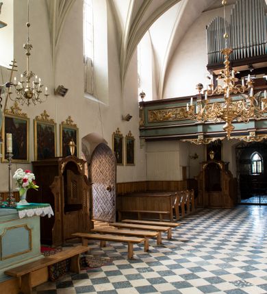 Zdjęcie nr 96: Kościół jest zlokalizowany na wzgórzu, w centrum wsi. Murowany z cegły, w wątku polskim, z zendrówką. Kościół jest orientowany, założony na planie prostokąta, jednonawowy, trójprzęsłowy, z dobudowanymi kruchtami od zachodu i południa. Prezbiterium oddzielone od nawy łukiem tęczowym, dwuprzęsłowe na planie prostokąta, zamknięte prostą ścianą, z dwukondygnacyjną przybudówką zakończoną trójbocznie. Nawa została przykryta sklepieniem sieciowym. Ściana południowa nawy przepruta trzema prostokątnymi oknami, zamkniętymi łukiem ostrym. Okna w nawie i prezbiterium dwudzielne, z sześcioma mniejszymi kwaterami. Przybudówka przy prezbiterium na parterze mieści zakrystię, a na piętrze składzik. Kruchta południowa sklepiona kolebką. Z kruchty do nawy prowadzi ostrołukowy, kamienny portal o dwóch archiwoltach. Kruchta zachodnia, obecnie kaplica św. Franciszka, sklepiona spłaszczoną, ukrytą kopułą na pendentywach. Ściana zachodnia kruchty przepruta dwoma ostrołukowymi oknami i ponad nimi okrągłym oknem. Od południa ostrołukowe wejście. Kościół o zróżnicowanej wysokości nawy i prezbiterium. Ściany opięte szkarpami. Na jednej trzeciej wysokości ścian oraz w zwieńczeniu nawy i prezbiterium profilowany gzyms. Od zachodu wklęsło-wypukły szczyt. Nawa, prezbiterium i dwie kruchty przykryte dachem dwuspadowym. Nad drugim przęsłem prezbiterium wieżyczka na sygnaturkę na planie ośmioboku, z profilowanym gzymsem i latarnią, zwieńczoną hełmem z kulą i krzyżem. Wejście do kościoła od południa i zachodu. Okna nawy i prezbiterium z kamiennym obramieniem. Nad wejściem do kruchty południowej formowany w cegle ostry łuk. Analogiczny łuk nad oknami w ścianie zachodniej i nad blendą w ścianie północnej. W przybudówce do prezbiterium dwie kondygnacje okien zamkniętych łukiem ostrym. W ścianie frontowej prostokątne wejście, a nad nim półkoliście zamknięta wnęka z grupą Ukrzyżowania. 


