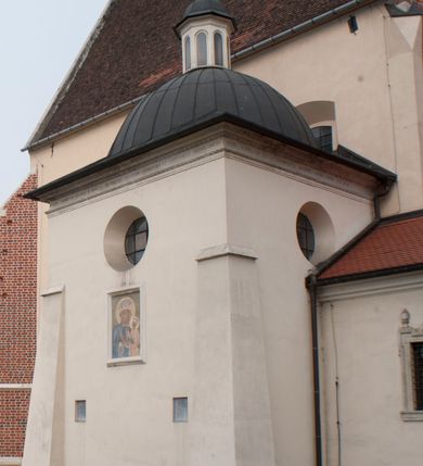 Zdjęcie nr 55: Kaplica pod wezwaniem Najświętszej Marii Panny i Wszystkich Świętych przylega do kościoła od południa, do pierwszego przęsła nawy, z którą komunikuje się za pomocą półkoliście zamkniętej arkady. Zbudowana została na planie kwadratu. Nakryto ją półsferyczną czaszą na pendentywach i zwieńczono latarnią. Wnętrze artykułowano za pomocą ślepej arkady z pilastrami i archiwoltami, ozdobionymi rzeźbioną dekoracją roślinną i kasetonami z rozetami w podłuczu. Ściany kaplicy zamyka wydatne belkowanie z fryzem i łacińską inskrypcją: "DEVS MEVS ET OMNIA / DILEXI DOMINE DECOREM DOMVS / TUAE ET LOCUM HABITATIONIS GLORAE TUAE PSAL(MUS) XXV". Na czterech pendentywach umieszczono stiukowe kartusze, z czego dwa od strony wschodniej są są puste, a dwa od strony zachodniej wypełniają herby skwadrowane: Gryf, Kotwicz, Kotwicz, Zabawa i Jastrzębiec, Nowina, Gozdawa, Pobóg. Wnętrze doświetlają trzy takie same okulusy umieszczone na każdej ze ścian. Czwarty okulus w ścianie północnej jest zaślepiony. Glify okulusów dekorowane są kasetonami z rozetami. Ściany kaplicy oraz wnętrze kopuły i latarni pokrywa polichromia figuralna. Po arkadą na ścianie wschodniej zawieszono obraz Matki Boskiej z Dzieciątkiem w bogato rzeźbionej roślinno-kwiatowej ramie zwieńczonej godłem z dwiema skrzyżowanymi laskami marszałkowskimi. Pod obrazem znajduje się nagrobek dziecięcy Jana Czuryły (zm. 1560) w formie płaskorzeźbionej, prostokątnej płyty z wyobrażeniem zmarłego. Nad płytą zlokalizowano mniejszą z inskrypcją odnoszącą się do zmarłego. Z kolei wnętrze arkady z herbem Gryf w kluczu na ścianie południowej wypełnia trójosiowy nagrobek Branickich z półokrągłym zwieńczeniem. Natomiast w arkadzie zachodniej wyobrażono scenę Zdjęcia z krzyża w formie malowidła ściennego. Wyposażenie wnętrza dopełniają dwie drewniane ławy kościelne. Ściany zewnętrzne wspierają dwie niskie przypory widoczne w narożach kaplicy. Całość zakończona jest belkowaniem z fryzem zawierającym inskrypcję: "AD LAVDEM DEI OPT(IMO) M(AXIMO) BEATEQUE GENITRICIS MARIAE VIRGINIS ET OMNIUM SANCTORU(M) HONOREM JOHANNES A RVSCZA BRANICZKI VENATOR CRACOVIEN(SIS) ET CAPITANEVS NIEPOLONICEN(SIS) - HANC CAPELLAM EX FVNDAMENTIS EREXIT ANNO D(OMI)NI 1596". Na ścianie południowej widnieje półokrągła blenda z malowanym przedstawieniem Matki Boskiej Częstochowskiej. Latarnię kaplicy wieńczy głowica z czterema maskami maszkaronów, na której wspiera się złocona kula z krzyżem.