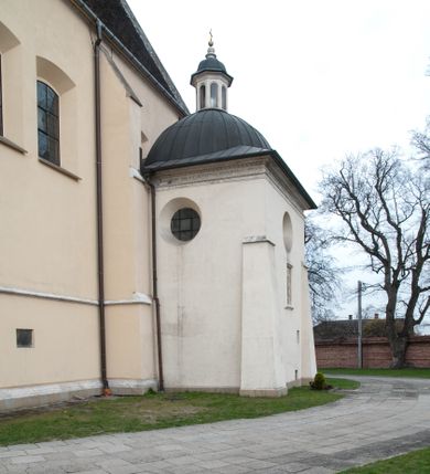 Zdjęcie nr 57: Kaplica pod wezwaniem Najświętszej Marii Panny i Wszystkich Świętych przylega do kościoła od południa, do pierwszego przęsła nawy, z którą komunikuje się za pomocą półkoliście zamkniętej arkady. Zbudowana została na planie kwadratu. Nakryto ją półsferyczną czaszą na pendentywach i zwieńczono latarnią. Wnętrze artykułowano za pomocą ślepej arkady z pilastrami i archiwoltami, ozdobionymi rzeźbioną dekoracją roślinną i kasetonami z rozetami w podłuczu. Ściany kaplicy zamyka wydatne belkowanie z fryzem i łacińską inskrypcją: "DEVS MEVS ET OMNIA / DILEXI DOMINE DECOREM DOMVS / TUAE ET LOCUM HABITATIONIS GLORAE TUAE PSAL(MUS) XXV". Na czterech pendentywach umieszczono stiukowe kartusze, z czego dwa od strony wschodniej są są puste, a dwa od strony zachodniej wypełniają herby skwadrowane: Gryf, Kotwicz, Kotwicz, Zabawa i Jastrzębiec, Nowina, Gozdawa, Pobóg. Wnętrze doświetlają trzy takie same okulusy umieszczone na każdej ze ścian. Czwarty okulus w ścianie północnej jest zaślepiony. Glify okulusów dekorowane są kasetonami z rozetami. Ściany kaplicy oraz wnętrze kopuły i latarni pokrywa polichromia figuralna. Po arkadą na ścianie wschodniej zawieszono obraz Matki Boskiej z Dzieciątkiem w bogato rzeźbionej roślinno-kwiatowej ramie zwieńczonej godłem z dwiema skrzyżowanymi laskami marszałkowskimi. Pod obrazem znajduje się nagrobek dziecięcy Jana Czuryły (zm. 1560) w formie płaskorzeźbionej, prostokątnej płyty z wyobrażeniem zmarłego. Nad płytą zlokalizowano mniejszą z inskrypcją odnoszącą się do zmarłego. Z kolei wnętrze arkady z herbem Gryf w kluczu na ścianie południowej wypełnia trójosiowy nagrobek Branickich z półokrągłym zwieńczeniem. Natomiast w arkadzie zachodniej wyobrażono scenę Zdjęcia z krzyża w formie malowidła ściennego. Wyposażenie wnętrza dopełniają dwie drewniane ławy kościelne. Ściany zewnętrzne wspierają dwie niskie przypory widoczne w narożach kaplicy. Całość zakończona jest belkowaniem z fryzem zawierającym inskrypcję: "AD LAVDEM DEI OPT(IMO) M(AXIMO) BEATEQUE GENITRICIS MARIAE VIRGINIS ET OMNIUM SANCTORU(M) HONOREM JOHANNES A RVSCZA BRANICZKI VENATOR CRACOVIEN(SIS) ET CAPITANEVS NIEPOLONICEN(SIS) - HANC CAPELLAM EX FVNDAMENTIS EREXIT ANNO D(OMI)NI 1596". Na ścianie południowej widnieje półokrągła blenda z malowanym przedstawieniem Matki Boskiej Częstochowskiej. Latarnię kaplicy wieńczy głowica z czterema maskami maszkaronów, na której wspiera się złocona kula z krzyżem.