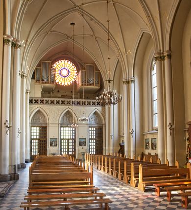 Zdjęcie nr 86: Kościół z cegły i kamienia. Na rzucie krzyża łacińskiego, jednonawowy z wciągniętymi do wnętrza przyporami. Prezbiterium krótkie, zamknięte pięcioma bokami ośmioboku. Korpus jednonawowy, czteroprzęsłowy, po bokach z płytkimi wnękami-kaplicami pomiędzy przyporami, poprzedzony od zach. przedsionkiem. Do pierwszego przęsła dostawione dwie symetryczne, trójboczne kaplice, nad nimi dwie czworoboczne wieże. Zakrystia przy prezbiterium na osi kościoła. Artykulacja ścian wnętrza za pomocą filarów opiętych półkolumnami z kapitelami z motywów liści. Między filarami rozpięte ostrołukowe arkady tworzące płytkie wnęki. Pierwsze przęsło wyróżnione przy pomocy masywnych filarów, ujętych niemal pełnoplastycznymi kolumnami. Okna ostrołukowe, dwudzielne z maswerkami, wsparte na gzymsach. Sklepienia krzyżowo-żebrowe na zaostrzonych gurtach. Kaplice artykułowane analogicznie do nawy kościoła, ze sklepieniami gwiaździstymi. Przedsionek otwiera się do kościoła trzema portalami ostrołukowymi opiętymi kolumnami. W polach archiwolt płaskorzeźby: Boże Narodzenie, Ukrzyżowanie, Wniebowstąpienie (K. Ceptowski).  W prezbiterium, na osi kościoła prostokątny otwór drzwiowy prowadzący do zakrystii. Chór muzyczny umieszczony nad kruchtą kościoła, na rzucie prostokąta, z kamienną balustradą maswerkową. Fasada kamienna, trójosiowa, zamknięta trójkątnie, flankowana lizenami przechodzącymi w ażurowe wieżyczki-latarnie, na rzucie kwadratu. Wieżyczki zwieńczone gzymsem i balustradą arkadową, hełmy ostrosłupowy zakończony iglicą. W dolnej części trzy filarowe arkady ostrołukowe, otwierające się do kruchty, sklepienie kruchty krzyżowo-żebrowe. Nad arkadami wejściowymi trzy tonda: litery IHS, Oko Opatrzności i splecione litery imienia Maria. Pośrodku na osi kościoła duża rozeta z maswerkiem, profilowana, otoczona pierścieniem wypełnionym stylizowanym ornamentem roślinnym. Ponad arkadami pełnoplastyczne figury czterech ewangelistów ustawionych na konsolach z rzeźbionymi atrybutami (F. Kuhn). Po bokach rozety prostokątne płyciny z traczami herbowymi Potockich i Branickich. U góry, na osi fasady figura Archanioła Michała. Elewacje na kamiennym cokole, z gzymsem kapnikowym, opięte prostokątnymi przyporami zwieńczonymi kamiennymi nakrywami. W górnej części kamienny fryz arkadkowy. Nad nim gzyms koronujący podtrzymujący ażurową, arkadową balustradę. Przy prezbiterium kaplice zamknięte trójbocznie, prezbiterium zamknięte pięciobocznie. Zakrystia na osi prezbiterium, na rzucie prostokąta, zwieńczona sygnaturką i ceglanym kominem. Po bokach prostokątne aneksy, południowy aneks - trzy okna ostrołukowe w kamiennej opasce, w środkowym przedstawienie Ukrzyżowanego Chrystusa. W północnym aneksie pojedyncze analogiczne okno. Okna ostrołukowe w profilowanych kamiennych opaskach, pomiędzy nimi a gzymsem koronującym mniejsze ostrołukowe w uskokowych arkadach. Nad kaplicami bocznymi dwie symetryczne wieże na rzucie kwadratu, w połowie wysokości kamienny gzyms z fryzem arkadkowym. Okna ostrołukowe w kamiennej opasce. Całość zwieńczona ślepym fryzem arkadkowym, wyżej gzyms dźwigający ażurową arkadkową balustradę. Hełmy ostrosłupowe, miedziane. Zakrystia na rzucie prostokąta, nakryta sklepieniem kolebkowym zaostrzonym i krzyżowym z lunetami , oddzielone gurtem. Portale od wschodu i zachodu prostokątne zamknięte łukiem ostrym. Okna ostrołukowe.