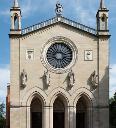 Zdjęcie nr 13: Kościół z cegły i kamienia. Na rzucie krzyża łacińskiego, jednonawowy z wciągniętymi do wnętrza przyporami. Prezbiterium krótkie, zamknięte pięcioma bokami ośmioboku. Korpus jednonawowy, czteroprzęsłowy, po bokach z płytkimi wnękami-kaplicami pomiędzy przyporami, poprzedzony od zach. przedsionkiem. Do pierwszego przęsła dostawione dwie symetryczne, trójboczne kaplice, nad nimi dwie czworoboczne wieże. Zakrystia przy prezbiterium na osi kościoła. Artykulacja ścian wnętrza za pomocą filarów opiętych półkolumnami z kapitelami z motywów liści. Między filarami rozpięte ostrołukowe arkady tworzące płytkie wnęki. Pierwsze przęsło wyróżnione przy pomocy masywnych filarów, ujętych niemal pełnoplastycznymi kolumnami. Okna ostrołukowe, dwudzielne z maswerkami, wsparte na gzymsach. Sklepienia krzyżowo-żebrowe na zaostrzonych gurtach. Kaplice artykułowane analogicznie do nawy kościoła, ze sklepieniami gwiaździstymi. Przedsionek otwiera się do kościoła trzema portalami ostrołukowymi opiętymi kolumnami. W polach archiwolt płaskorzeźby: Boże Narodzenie, Ukrzyżowanie, Wniebowstąpienie (K. Ceptowski).  W prezbiterium, na osi kościoła prostokątny otwór drzwiowy prowadzący do zakrystii. Chór muzyczny umieszczony nad kruchtą kościoła, na rzucie prostokąta, z kamienną balustradą maswerkową. Fasada kamienna, trójosiowa, zamknięta trójkątnie, flankowana lizenami przechodzącymi w ażurowe wieżyczki-latarnie, na rzucie kwadratu. Wieżyczki zwieńczone gzymsem i balustradą arkadową, hełmy ostrosłupowy zakończony iglicą. W dolnej części trzy filarowe arkady ostrołukowe, otwierające się do kruchty, sklepienie kruchty krzyżowo-żebrowe. Nad arkadami wejściowymi trzy tonda: litery IHS, Oko Opatrzności i splecione litery imienia Maria. Pośrodku na osi kościoła duża rozeta z maswerkiem, profilowana, otoczona pierścieniem wypełnionym stylizowanym ornamentem roślinnym. Ponad arkadami pełnoplastyczne figury czterech ewangelistów ustawionych na konsolach z rzeźbionymi atrybutami (F. Kuhn). Po bokach rozety prostokątne płyciny z traczami herbowymi Potockich i Branickich. U góry, na osi fasady figura Archanioła Michała. Elewacje na kamiennym cokole, z gzymsem kapnikowym, opięte prostokątnymi przyporami zwieńczonymi kamiennymi nakrywami. W górnej części kamienny fryz arkadkowy. Nad nim gzyms koronujący podtrzymujący ażurową, arkadową balustradę. Przy prezbiterium kaplice zamknięte trójbocznie, prezbiterium zamknięte pięciobocznie. Zakrystia na osi prezbiterium, na rzucie prostokąta, zwieńczona sygnaturką i ceglanym kominem. Po bokach prostokątne aneksy, południowy aneks - trzy okna ostrołukowe w kamiennej opasce, w środkowym przedstawienie Ukrzyżowanego Chrystusa. W północnym aneksie pojedyncze analogiczne okno. Okna ostrołukowe w profilowanych kamiennych opaskach, pomiędzy nimi a gzymsem koronującym mniejsze ostrołukowe w uskokowych arkadach. Nad kaplicami bocznymi dwie symetryczne wieże na rzucie kwadratu, w połowie wysokości kamienny gzyms z fryzem arkadkowym. Okna ostrołukowe w kamiennej opasce. Całość zwieńczona ślepym fryzem arkadkowym, wyżej gzyms dźwigający ażurową arkadkową balustradę. Hełmy ostrosłupowe, miedziane. Zakrystia na rzucie prostokąta, nakryta sklepieniem kolebkowym zaostrzonym i krzyżowym z lunetami , oddzielone gurtem. Portale od wschodu i zachodu prostokątne zamknięte łukiem ostrym. Okna ostrołukowe.