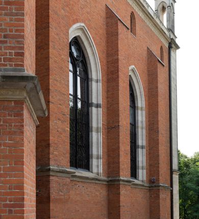 Zdjęcie nr 12: Kościół z cegły i kamienia. Na rzucie krzyża łacińskiego, jednonawowy z wciągniętymi do wnętrza przyporami. Prezbiterium krótkie, zamknięte pięcioma bokami ośmioboku. Korpus jednonawowy, czteroprzęsłowy, po bokach z płytkimi wnękami-kaplicami pomiędzy przyporami, poprzedzony od zach. przedsionkiem. Do pierwszego przęsła dostawione dwie symetryczne, trójboczne kaplice, nad nimi dwie czworoboczne wieże. Zakrystia przy prezbiterium na osi kościoła. Artykulacja ścian wnętrza za pomocą filarów opiętych półkolumnami z kapitelami z motywów liści. Między filarami rozpięte ostrołukowe arkady tworzące płytkie wnęki. Pierwsze przęsło wyróżnione przy pomocy masywnych filarów, ujętych niemal pełnoplastycznymi kolumnami. Okna ostrołukowe, dwudzielne z maswerkami, wsparte na gzymsach. Sklepienia krzyżowo-żebrowe na zaostrzonych gurtach. Kaplice artykułowane analogicznie do nawy kościoła, ze sklepieniami gwiaździstymi. Przedsionek otwiera się do kościoła trzema portalami ostrołukowymi opiętymi kolumnami. W polach archiwolt płaskorzeźby: Boże Narodzenie, Ukrzyżowanie, Wniebowstąpienie (K. Ceptowski).  W prezbiterium, na osi kościoła prostokątny otwór drzwiowy prowadzący do zakrystii. Chór muzyczny umieszczony nad kruchtą kościoła, na rzucie prostokąta, z kamienną balustradą maswerkową. Fasada kamienna, trójosiowa, zamknięta trójkątnie, flankowana lizenami przechodzącymi w ażurowe wieżyczki-latarnie, na rzucie kwadratu. Wieżyczki zwieńczone gzymsem i balustradą arkadową, hełmy ostrosłupowy zakończony iglicą. W dolnej części trzy filarowe arkady ostrołukowe, otwierające się do kruchty, sklepienie kruchty krzyżowo-żebrowe. Nad arkadami wejściowymi trzy tonda: litery IHS, Oko Opatrzności i splecione litery imienia Maria. Pośrodku na osi kościoła duża rozeta z maswerkiem, profilowana, otoczona pierścieniem wypełnionym stylizowanym ornamentem roślinnym. Ponad arkadami pełnoplastyczne figury czterech ewangelistów ustawionych na konsolach z rzeźbionymi atrybutami (F. Kuhn). Po bokach rozety prostokątne płyciny z traczami herbowymi Potockich i Branickich. U góry, na osi fasady figura Archanioła Michała. Elewacje na kamiennym cokole, z gzymsem kapnikowym, opięte prostokątnymi przyporami zwieńczonymi kamiennymi nakrywami. W górnej części kamienny fryz arkadkowy. Nad nim gzyms koronujący podtrzymujący ażurową, arkadową balustradę. Przy prezbiterium kaplice zamknięte trójbocznie, prezbiterium zamknięte pięciobocznie. Zakrystia na osi prezbiterium, na rzucie prostokąta, zwieńczona sygnaturką i ceglanym kominem. Po bokach prostokątne aneksy, południowy aneks - trzy okna ostrołukowe w kamiennej opasce, w środkowym przedstawienie Ukrzyżowanego Chrystusa. W północnym aneksie pojedyncze analogiczne okno. Okna ostrołukowe w profilowanych kamiennych opaskach, pomiędzy nimi a gzymsem koronującym mniejsze ostrołukowe w uskokowych arkadach. Nad kaplicami bocznymi dwie symetryczne wieże na rzucie kwadratu, w połowie wysokości kamienny gzyms z fryzem arkadkowym. Okna ostrołukowe w kamiennej opasce. Całość zwieńczona ślepym fryzem arkadkowym, wyżej gzyms dźwigający ażurową arkadkową balustradę. Hełmy ostrosłupowe, miedziane. Zakrystia na rzucie prostokąta, nakryta sklepieniem kolebkowym zaostrzonym i krzyżowym z lunetami , oddzielone gurtem. Portale od wschodu i zachodu prostokątne zamknięte łukiem ostrym. Okna ostrołukowe.