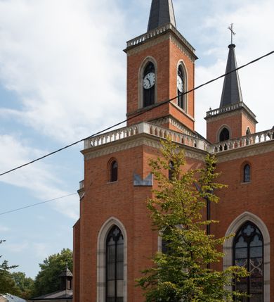 Zdjęcie nr 88: Kościół z cegły i kamienia. Na rzucie krzyża łacińskiego, jednonawowy z wciągniętymi do wnętrza przyporami. Prezbiterium krótkie, zamknięte pięcioma bokami ośmioboku. Korpus jednonawowy, czteroprzęsłowy, po bokach z płytkimi wnękami-kaplicami pomiędzy przyporami, poprzedzony od zach. przedsionkiem. Do pierwszego przęsła dostawione dwie symetryczne, trójboczne kaplice, nad nimi dwie czworoboczne wieże. Zakrystia przy prezbiterium na osi kościoła. Artykulacja ścian wnętrza za pomocą filarów opiętych półkolumnami z kapitelami z motywów liści. Między filarami rozpięte ostrołukowe arkady tworzące płytkie wnęki. Pierwsze przęsło wyróżnione przy pomocy masywnych filarów, ujętych niemal pełnoplastycznymi kolumnami. Okna ostrołukowe, dwudzielne z maswerkami, wsparte na gzymsach. Sklepienia krzyżowo-żebrowe na zaostrzonych gurtach. Kaplice artykułowane analogicznie do nawy kościoła, ze sklepieniami gwiaździstymi. Przedsionek otwiera się do kościoła trzema portalami ostrołukowymi opiętymi kolumnami. W polach archiwolt płaskorzeźby: Boże Narodzenie, Ukrzyżowanie, Wniebowstąpienie (K. Ceptowski).  W prezbiterium, na osi kościoła prostokątny otwór drzwiowy prowadzący do zakrystii. Chór muzyczny umieszczony nad kruchtą kościoła, na rzucie prostokąta, z kamienną balustradą maswerkową. Fasada kamienna, trójosiowa, zamknięta trójkątnie, flankowana lizenami przechodzącymi w ażurowe wieżyczki-latarnie, na rzucie kwadratu. Wieżyczki zwieńczone gzymsem i balustradą arkadową, hełmy ostrosłupowy zakończony iglicą. W dolnej części trzy filarowe arkady ostrołukowe, otwierające się do kruchty, sklepienie kruchty krzyżowo-żebrowe. Nad arkadami wejściowymi trzy tonda: litery IHS, Oko Opatrzności i splecione litery imienia Maria. Pośrodku na osi kościoła duża rozeta z maswerkiem, profilowana, otoczona pierścieniem wypełnionym stylizowanym ornamentem roślinnym. Ponad arkadami pełnoplastyczne figury czterech ewangelistów ustawionych na konsolach z rzeźbionymi atrybutami (F. Kuhn). Po bokach rozety prostokątne płyciny z traczami herbowymi Potockich i Branickich. U góry, na osi fasady figura Archanioła Michała. Elewacje na kamiennym cokole, z gzymsem kapnikowym, opięte prostokątnymi przyporami zwieńczonymi kamiennymi nakrywami. W górnej części kamienny fryz arkadkowy. Nad nim gzyms koronujący podtrzymujący ażurową, arkadową balustradę. Przy prezbiterium kaplice zamknięte trójbocznie, prezbiterium zamknięte pięciobocznie. Zakrystia na osi prezbiterium, na rzucie prostokąta, zwieńczona sygnaturką i ceglanym kominem. Po bokach prostokątne aneksy, południowy aneks - trzy okna ostrołukowe w kamiennej opasce, w środkowym przedstawienie Ukrzyżowanego Chrystusa. W północnym aneksie pojedyncze analogiczne okno. Okna ostrołukowe w profilowanych kamiennych opaskach, pomiędzy nimi a gzymsem koronującym mniejsze ostrołukowe w uskokowych arkadach. Nad kaplicami bocznymi dwie symetryczne wieże na rzucie kwadratu, w połowie wysokości kamienny gzyms z fryzem arkadkowym. Okna ostrołukowe w kamiennej opasce. Całość zwieńczona ślepym fryzem arkadkowym, wyżej gzyms dźwigający ażurową arkadkową balustradę. Hełmy ostrosłupowe, miedziane. Zakrystia na rzucie prostokąta, nakryta sklepieniem kolebkowym zaostrzonym i krzyżowym z lunetami , oddzielone gurtem. Portale od wschodu i zachodu prostokątne zamknięte łukiem ostrym. Okna ostrołukowe.