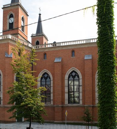Zdjęcie nr 57: Kościół z cegły i kamienia. Na rzucie krzyża łacińskiego, jednonawowy z wciągniętymi do wnętrza przyporami. Prezbiterium krótkie, zamknięte pięcioma bokami ośmioboku. Korpus jednonawowy, czteroprzęsłowy, po bokach z płytkimi wnękami-kaplicami pomiędzy przyporami, poprzedzony od zach. przedsionkiem. Do pierwszego przęsła dostawione dwie symetryczne, trójboczne kaplice, nad nimi dwie czworoboczne wieże. Zakrystia przy prezbiterium na osi kościoła. Artykulacja ścian wnętrza za pomocą filarów opiętych półkolumnami z kapitelami z motywów liści. Między filarami rozpięte ostrołukowe arkady tworzące płytkie wnęki. Pierwsze przęsło wyróżnione przy pomocy masywnych filarów, ujętych niemal pełnoplastycznymi kolumnami. Okna ostrołukowe, dwudzielne z maswerkami, wsparte na gzymsach. Sklepienia krzyżowo-żebrowe na zaostrzonych gurtach. Kaplice artykułowane analogicznie do nawy kościoła, ze sklepieniami gwiaździstymi. Przedsionek otwiera się do kościoła trzema portalami ostrołukowymi opiętymi kolumnami. W polach archiwolt płaskorzeźby: Boże Narodzenie, Ukrzyżowanie, Wniebowstąpienie (K. Ceptowski).  W prezbiterium, na osi kościoła prostokątny otwór drzwiowy prowadzący do zakrystii. Chór muzyczny umieszczony nad kruchtą kościoła, na rzucie prostokąta, z kamienną balustradą maswerkową. Fasada kamienna, trójosiowa, zamknięta trójkątnie, flankowana lizenami przechodzącymi w ażurowe wieżyczki-latarnie, na rzucie kwadratu. Wieżyczki zwieńczone gzymsem i balustradą arkadową, hełmy ostrosłupowy zakończony iglicą. W dolnej części trzy filarowe arkady ostrołukowe, otwierające się do kruchty, sklepienie kruchty krzyżowo-żebrowe. Nad arkadami wejściowymi trzy tonda: litery IHS, Oko Opatrzności i splecione litery imienia Maria. Pośrodku na osi kościoła duża rozeta z maswerkiem, profilowana, otoczona pierścieniem wypełnionym stylizowanym ornamentem roślinnym. Ponad arkadami pełnoplastyczne figury czterech ewangelistów ustawionych na konsolach z rzeźbionymi atrybutami (F. Kuhn). Po bokach rozety prostokątne płyciny z traczami herbowymi Potockich i Branickich. U góry, na osi fasady figura Archanioła Michała. Elewacje na kamiennym cokole, z gzymsem kapnikowym, opięte prostokątnymi przyporami zwieńczonymi kamiennymi nakrywami. W górnej części kamienny fryz arkadkowy. Nad nim gzyms koronujący podtrzymujący ażurową, arkadową balustradę. Przy prezbiterium kaplice zamknięte trójbocznie, prezbiterium zamknięte pięciobocznie. Zakrystia na osi prezbiterium, na rzucie prostokąta, zwieńczona sygnaturką i ceglanym kominem. Po bokach prostokątne aneksy, południowy aneks - trzy okna ostrołukowe w kamiennej opasce, w środkowym przedstawienie Ukrzyżowanego Chrystusa. W północnym aneksie pojedyncze analogiczne okno. Okna ostrołukowe w profilowanych kamiennych opaskach, pomiędzy nimi a gzymsem koronującym mniejsze ostrołukowe w uskokowych arkadach. Nad kaplicami bocznymi dwie symetryczne wieże na rzucie kwadratu, w połowie wysokości kamienny gzyms z fryzem arkadkowym. Okna ostrołukowe w kamiennej opasce. Całość zwieńczona ślepym fryzem arkadkowym, wyżej gzyms dźwigający ażurową arkadkową balustradę. Hełmy ostrosłupowe, miedziane. Zakrystia na rzucie prostokąta, nakryta sklepieniem kolebkowym zaostrzonym i krzyżowym z lunetami , oddzielone gurtem. Portale od wschodu i zachodu prostokątne zamknięte łukiem ostrym. Okna ostrołukowe.