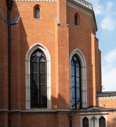 Zdjęcie nr 11: Kościół z cegły i kamienia. Na rzucie krzyża łacińskiego, jednonawowy z wciągniętymi do wnętrza przyporami. Prezbiterium krótkie, zamknięte pięcioma bokami ośmioboku. Korpus jednonawowy, czteroprzęsłowy, po bokach z płytkimi wnękami-kaplicami pomiędzy przyporami, poprzedzony od zach. przedsionkiem. Do pierwszego przęsła dostawione dwie symetryczne, trójboczne kaplice, nad nimi dwie czworoboczne wieże. Zakrystia przy prezbiterium na osi kościoła. Artykulacja ścian wnętrza za pomocą filarów opiętych półkolumnami z kapitelami z motywów liści. Między filarami rozpięte ostrołukowe arkady tworzące płytkie wnęki. Pierwsze przęsło wyróżnione przy pomocy masywnych filarów, ujętych niemal pełnoplastycznymi kolumnami. Okna ostrołukowe, dwudzielne z maswerkami, wsparte na gzymsach. Sklepienia krzyżowo-żebrowe na zaostrzonych gurtach. Kaplice artykułowane analogicznie do nawy kościoła, ze sklepieniami gwiaździstymi. Przedsionek otwiera się do kościoła trzema portalami ostrołukowymi opiętymi kolumnami. W polach archiwolt płaskorzeźby: Boże Narodzenie, Ukrzyżowanie, Wniebowstąpienie (K. Ceptowski).  W prezbiterium, na osi kościoła prostokątny otwór drzwiowy prowadzący do zakrystii. Chór muzyczny umieszczony nad kruchtą kościoła, na rzucie prostokąta, z kamienną balustradą maswerkową. Fasada kamienna, trójosiowa, zamknięta trójkątnie, flankowana lizenami przechodzącymi w ażurowe wieżyczki-latarnie, na rzucie kwadratu. Wieżyczki zwieńczone gzymsem i balustradą arkadową, hełmy ostrosłupowy zakończony iglicą. W dolnej części trzy filarowe arkady ostrołukowe, otwierające się do kruchty, sklepienie kruchty krzyżowo-żebrowe. Nad arkadami wejściowymi trzy tonda: litery IHS, Oko Opatrzności i splecione litery imienia Maria. Pośrodku na osi kościoła duża rozeta z maswerkiem, profilowana, otoczona pierścieniem wypełnionym stylizowanym ornamentem roślinnym. Ponad arkadami pełnoplastyczne figury czterech ewangelistów ustawionych na konsolach z rzeźbionymi atrybutami (F. Kuhn). Po bokach rozety prostokątne płyciny z traczami herbowymi Potockich i Branickich. U góry, na osi fasady figura Archanioła Michała. Elewacje na kamiennym cokole, z gzymsem kapnikowym, opięte prostokątnymi przyporami zwieńczonymi kamiennymi nakrywami. W górnej części kamienny fryz arkadkowy. Nad nim gzyms koronujący podtrzymujący ażurową, arkadową balustradę. Przy prezbiterium kaplice zamknięte trójbocznie, prezbiterium zamknięte pięciobocznie. Zakrystia na osi prezbiterium, na rzucie prostokąta, zwieńczona sygnaturką i ceglanym kominem. Po bokach prostokątne aneksy, południowy aneks - trzy okna ostrołukowe w kamiennej opasce, w środkowym przedstawienie Ukrzyżowanego Chrystusa. W północnym aneksie pojedyncze analogiczne okno. Okna ostrołukowe w profilowanych kamiennych opaskach, pomiędzy nimi a gzymsem koronującym mniejsze ostrołukowe w uskokowych arkadach. Nad kaplicami bocznymi dwie symetryczne wieże na rzucie kwadratu, w połowie wysokości kamienny gzyms z fryzem arkadkowym. Okna ostrołukowe w kamiennej opasce. Całość zwieńczona ślepym fryzem arkadkowym, wyżej gzyms dźwigający ażurową arkadkową balustradę. Hełmy ostrosłupowe, miedziane. Zakrystia na rzucie prostokąta, nakryta sklepieniem kolebkowym zaostrzonym i krzyżowym z lunetami , oddzielone gurtem. Portale od wschodu i zachodu prostokątne zamknięte łukiem ostrym. Okna ostrołukowe.