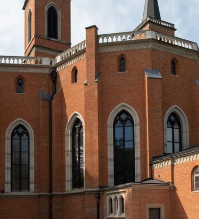 Zdjęcie nr 10: Kościół z cegły i kamienia. Na rzucie krzyża łacińskiego, jednonawowy z wciągniętymi do wnętrza przyporami. Prezbiterium krótkie, zamknięte pięcioma bokami ośmioboku. Korpus jednonawowy, czteroprzęsłowy, po bokach z płytkimi wnękami-kaplicami pomiędzy przyporami, poprzedzony od zach. przedsionkiem. Do pierwszego przęsła dostawione dwie symetryczne, trójboczne kaplice, nad nimi dwie czworoboczne wieże. Zakrystia przy prezbiterium na osi kościoła. Artykulacja ścian wnętrza za pomocą filarów opiętych półkolumnami z kapitelami z motywów liści. Między filarami rozpięte ostrołukowe arkady tworzące płytkie wnęki. Pierwsze przęsło wyróżnione przy pomocy masywnych filarów, ujętych niemal pełnoplastycznymi kolumnami. Okna ostrołukowe, dwudzielne z maswerkami, wsparte na gzymsach. Sklepienia krzyżowo-żebrowe na zaostrzonych gurtach. Kaplice artykułowane analogicznie do nawy kościoła, ze sklepieniami gwiaździstymi. Przedsionek otwiera się do kościoła trzema portalami ostrołukowymi opiętymi kolumnami. W polach archiwolt płaskorzeźby: Boże Narodzenie, Ukrzyżowanie, Wniebowstąpienie (K. Ceptowski).  W prezbiterium, na osi kościoła prostokątny otwór drzwiowy prowadzący do zakrystii. Chór muzyczny umieszczony nad kruchtą kościoła, na rzucie prostokąta, z kamienną balustradą maswerkową. Fasada kamienna, trójosiowa, zamknięta trójkątnie, flankowana lizenami przechodzącymi w ażurowe wieżyczki-latarnie, na rzucie kwadratu. Wieżyczki zwieńczone gzymsem i balustradą arkadową, hełmy ostrosłupowy zakończony iglicą. W dolnej części trzy filarowe arkady ostrołukowe, otwierające się do kruchty, sklepienie kruchty krzyżowo-żebrowe. Nad arkadami wejściowymi trzy tonda: litery IHS, Oko Opatrzności i splecione litery imienia Maria. Pośrodku na osi kościoła duża rozeta z maswerkiem, profilowana, otoczona pierścieniem wypełnionym stylizowanym ornamentem roślinnym. Ponad arkadami pełnoplastyczne figury czterech ewangelistów ustawionych na konsolach z rzeźbionymi atrybutami (F. Kuhn). Po bokach rozety prostokątne płyciny z traczami herbowymi Potockich i Branickich. U góry, na osi fasady figura Archanioła Michała. Elewacje na kamiennym cokole, z gzymsem kapnikowym, opięte prostokątnymi przyporami zwieńczonymi kamiennymi nakrywami. W górnej części kamienny fryz arkadkowy. Nad nim gzyms koronujący podtrzymujący ażurową, arkadową balustradę. Przy prezbiterium kaplice zamknięte trójbocznie, prezbiterium zamknięte pięciobocznie. Zakrystia na osi prezbiterium, na rzucie prostokąta, zwieńczona sygnaturką i ceglanym kominem. Po bokach prostokątne aneksy, południowy aneks - trzy okna ostrołukowe w kamiennej opasce, w środkowym przedstawienie Ukrzyżowanego Chrystusa. W północnym aneksie pojedyncze analogiczne okno. Okna ostrołukowe w profilowanych kamiennych opaskach, pomiędzy nimi a gzymsem koronującym mniejsze ostrołukowe w uskokowych arkadach. Nad kaplicami bocznymi dwie symetryczne wieże na rzucie kwadratu, w połowie wysokości kamienny gzyms z fryzem arkadkowym. Okna ostrołukowe w kamiennej opasce. Całość zwieńczona ślepym fryzem arkadkowym, wyżej gzyms dźwigający ażurową arkadkową balustradę. Hełmy ostrosłupowe, miedziane. Zakrystia na rzucie prostokąta, nakryta sklepieniem kolebkowym zaostrzonym i krzyżowym z lunetami , oddzielone gurtem. Portale od wschodu i zachodu prostokątne zamknięte łukiem ostrym. Okna ostrołukowe.