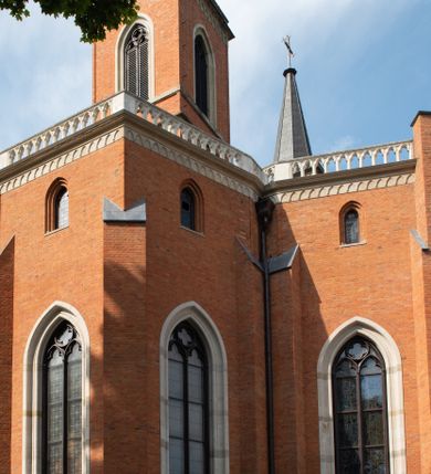 Zdjęcie nr 18: Kościół z cegły i kamienia. Na rzucie krzyża łacińskiego, jednonawowy z wciągniętymi do wnętrza przyporami. Prezbiterium krótkie, zamknięte pięcioma bokami ośmioboku. Korpus jednonawowy, czteroprzęsłowy, po bokach z płytkimi wnękami-kaplicami pomiędzy przyporami, poprzedzony od zach. przedsionkiem. Do pierwszego przęsła dostawione dwie symetryczne, trójboczne kaplice, nad nimi dwie czworoboczne wieże. Zakrystia przy prezbiterium na osi kościoła. Artykulacja ścian wnętrza za pomocą filarów opiętych półkolumnami z kapitelami z motywów liści. Między filarami rozpięte ostrołukowe arkady tworzące płytkie wnęki. Pierwsze przęsło wyróżnione przy pomocy masywnych filarów, ujętych niemal pełnoplastycznymi kolumnami. Okna ostrołukowe, dwudzielne z maswerkami, wsparte na gzymsach. Sklepienia krzyżowo-żebrowe na zaostrzonych gurtach. Kaplice artykułowane analogicznie do nawy kościoła, ze sklepieniami gwiaździstymi. Przedsionek otwiera się do kościoła trzema portalami ostrołukowymi opiętymi kolumnami. W polach archiwolt płaskorzeźby: Boże Narodzenie, Ukrzyżowanie, Wniebowstąpienie (K. Ceptowski).  W prezbiterium, na osi kościoła prostokątny otwór drzwiowy prowadzący do zakrystii. Chór muzyczny umieszczony nad kruchtą kościoła, na rzucie prostokąta, z kamienną balustradą maswerkową. Fasada kamienna, trójosiowa, zamknięta trójkątnie, flankowana lizenami przechodzącymi w ażurowe wieżyczki-latarnie, na rzucie kwadratu. Wieżyczki zwieńczone gzymsem i balustradą arkadową, hełmy ostrosłupowy zakończony iglicą. W dolnej części trzy filarowe arkady ostrołukowe, otwierające się do kruchty, sklepienie kruchty krzyżowo-żebrowe. Nad arkadami wejściowymi trzy tonda: litery IHS, Oko Opatrzności i splecione litery imienia Maria. Pośrodku na osi kościoła duża rozeta z maswerkiem, profilowana, otoczona pierścieniem wypełnionym stylizowanym ornamentem roślinnym. Ponad arkadami pełnoplastyczne figury czterech ewangelistów ustawionych na konsolach z rzeźbionymi atrybutami (F. Kuhn). Po bokach rozety prostokątne płyciny z traczami herbowymi Potockich i Branickich. U góry, na osi fasady figura Archanioła Michała. Elewacje na kamiennym cokole, z gzymsem kapnikowym, opięte prostokątnymi przyporami zwieńczonymi kamiennymi nakrywami. W górnej części kamienny fryz arkadkowy. Nad nim gzyms koronujący podtrzymujący ażurową, arkadową balustradę. Przy prezbiterium kaplice zamknięte trójbocznie, prezbiterium zamknięte pięciobocznie. Zakrystia na osi prezbiterium, na rzucie prostokąta, zwieńczona sygnaturką i ceglanym kominem. Po bokach prostokątne aneksy, południowy aneks - trzy okna ostrołukowe w kamiennej opasce, w środkowym przedstawienie Ukrzyżowanego Chrystusa. W północnym aneksie pojedyncze analogiczne okno. Okna ostrołukowe w profilowanych kamiennych opaskach, pomiędzy nimi a gzymsem koronującym mniejsze ostrołukowe w uskokowych arkadach. Nad kaplicami bocznymi dwie symetryczne wieże na rzucie kwadratu, w połowie wysokości kamienny gzyms z fryzem arkadkowym. Okna ostrołukowe w kamiennej opasce. Całość zwieńczona ślepym fryzem arkadkowym, wyżej gzyms dźwigający ażurową arkadkową balustradę. Hełmy ostrosłupowe, miedziane. Zakrystia na rzucie prostokąta, nakryta sklepieniem kolebkowym zaostrzonym i krzyżowym z lunetami , oddzielone gurtem. Portale od wschodu i zachodu prostokątne zamknięte łukiem ostrym. Okna ostrołukowe.