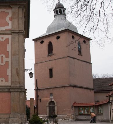 Zdjęcie nr 1: Dzwonnica murowana z cegły, tynkowana. Zbudowana na rzucie kwadratu, na cokole, trójkondygnacyjna, zwieńczona blaszanym hełmem z ażurową wieżyczką i iglicą. Od wschodu wejście, zamknięte łukiem półkolistym, w kamiennym, profilowanym obramieniu. Nad nim kamienna tarcza z herbem Lis. W najwyższej kondygnacji duże ostrołukowe otwory dzwonne, wyżej, pod okapem małe owalne.