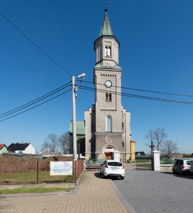 Zdjęcie nr 13: Budynki kościoła i plebanii znajdują się w centralnej części wsi, przy rynku na północ od głównej drogi z Krakowa do Oświęcimia. Kościół stoi przy obszernym placu, obwiedziony wysokim kamiennym murem z metalowym ogrodzeniem od południa. Kościół z prezbiterium zwróconym na północ, wzniesiony z kamienia wapiennego i cegły, tynkowany, z podmurówką. Świątynia wybudowana na planie krzyża łacińskiego z bazylikowym korpusem i transeptem. Dwuprzęsłowe prezbiterium zakończone półkoliście absydą zostało ujęte w dwa aneksy boczne, z których zachodni przeznaczony jest na zakrystię. Od południa do budynku przylega kruchta w przyziemiu wieży. Wnętrze kościoła trójnawowe, czteroprzęsłowe. Nawa główna łączy się z nawami bocznymi arkadami wspartymi na pięciobocznych filarach. Nawy boczne ujęte szerokimi pilastrami z pięciobocznymi filarami. Filary i pilastry stoją na wysokich, masywnych cokołach z kapitelami analogicznymi jak w nawie głównej. Ściany na skrzyżowaniu naw oraz ściany prezbiterium ujęte wspomnianymi filarami podtrzymującymi gurty sklepienia. Nawa i prezbiterium przykryte są sklepieniem kolebkowym z geometryzowanymi lunetami po obu stronach ścian. Ramiona transeptu sklepione kolebkowo z analogicznymi lunetami. Na skrzyżowaniu naw znajduje się sklepienie żaglaste. Nawę główną oświetlają rozmieszczone po jednym w każdym przęśle otwory okienne zamknięte łukiem półkolistym, okna w transepcie to biforia, widoczne tylko z zewnątrz okrągłe okno w absydzie wypełnione jest kamienną rozetą. Główne wejście od południa, do pierwszego przęsła od transeptu prowadzi dwoje drzwi w otworach o zamknięciu w kształcie łuku odciętego. W części zachodniej chór muzyczny wsparty na dwóch kolumnach i dwóch filarach dostawionych do ściany. Ich kapitele są analogiczne do pozostałych w kościele. Sklepienia dekorowane polichromią z rozetami i pękami lilii, a na skrzyżowaniu naw umieszczono malunek naścienny ukazujący Chrystusa tronującego z Bogiem Ojcem i gołębicą Ducha Świętego, a wokół nich cztery symbole ewangelistów. W fasadzie świątyni znajduje się strzelista wieża dwukondygnacyjna na planie czworokąta, przechodząca wyżej w ośmioboczną. Po bokach wieży wysokie aneksy zwieńczone schodkowo. Nad wejściem do kościoła znajduje się ozdobne okno zamknięte półkoliście i wypełnione czterema małymi rozetami ułożonymi jedna nad drugą. W kolejnej kondygnacji wieżę przepruwa biforium poniżej tarczy zegara i dekoracji arkadkowej. Wieża pełni jednocześnie funkcję dzwonnicy. Druga wieża na skrzyżowaniu nawy głównej i transeptu mieści sygnaturkę. Korpus kościoła nakryty dachem dwuspadowym, wieża wielobocznym. Wszystkie dachy kryte blachą.