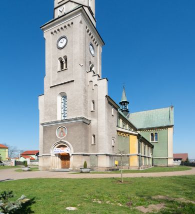 Zdjęcie nr 43: Budynki kościoła i plebanii znajdują się w centralnej części wsi, przy rynku na północ od głównej drogi z Krakowa do Oświęcimia. Kościół stoi przy obszernym placu, obwiedziony wysokim kamiennym murem z metalowym ogrodzeniem od południa. Kościół z prezbiterium zwróconym na północ, wzniesiony z kamienia wapiennego i cegły, tynkowany, z podmurówką. Świątynia wybudowana na planie krzyża łacińskiego z bazylikowym korpusem i transeptem. Dwuprzęsłowe prezbiterium zakończone półkoliście absydą zostało ujęte w dwa aneksy boczne, z których zachodni przeznaczony jest na zakrystię. Od południa do budynku przylega kruchta w przyziemiu wieży. Wnętrze kościoła trójnawowe, czteroprzęsłowe. Nawa główna łączy się z nawami bocznymi arkadami wspartymi na pięciobocznych filarach. Nawy boczne ujęte szerokimi pilastrami z pięciobocznymi filarami. Filary i pilastry stoją na wysokich, masywnych cokołach z kapitelami analogicznymi jak w nawie głównej. Ściany na skrzyżowaniu naw oraz ściany prezbiterium ujęte wspomnianymi filarami podtrzymującymi gurty sklepienia. Nawa i prezbiterium przykryte są sklepieniem kolebkowym z geometryzowanymi lunetami po obu stronach ścian. Ramiona transeptu sklepione kolebkowo z analogicznymi lunetami. Na skrzyżowaniu naw znajduje się sklepienie żaglaste. Nawę główną oświetlają rozmieszczone po jednym w każdym przęśle otwory okienne zamknięte łukiem półkolistym, okna w transepcie to biforia, widoczne tylko z zewnątrz okrągłe okno w absydzie wypełnione jest kamienną rozetą. Główne wejście od południa, do pierwszego przęsła od transeptu prowadzi dwoje drzwi w otworach o zamknięciu w kształcie łuku odciętego. W części zachodniej chór muzyczny wsparty na dwóch kolumnach i dwóch filarach dostawionych do ściany. Ich kapitele są analogiczne do pozostałych w kościele. Sklepienia dekorowane polichromią z rozetami i pękami lilii, a na skrzyżowaniu naw umieszczono malunek naścienny ukazujący Chrystusa tronującego z Bogiem Ojcem i gołębicą Ducha Świętego, a wokół nich cztery symbole ewangelistów. W fasadzie świątyni znajduje się strzelista wieża dwukondygnacyjna na planie czworokąta, przechodząca wyżej w ośmioboczną. Po bokach wieży wysokie aneksy zwieńczone schodkowo. Nad wejściem do kościoła znajduje się ozdobne okno zamknięte półkoliście i wypełnione czterema małymi rozetami ułożonymi jedna nad drugą. W kolejnej kondygnacji wieżę przepruwa biforium poniżej tarczy zegara i dekoracji arkadkowej. Wieża pełni jednocześnie funkcję dzwonnicy. Druga wieża na skrzyżowaniu nawy głównej i transeptu mieści sygnaturkę. Korpus kościoła nakryty dachem dwuspadowym, wieża wielobocznym. Wszystkie dachy kryte blachą.